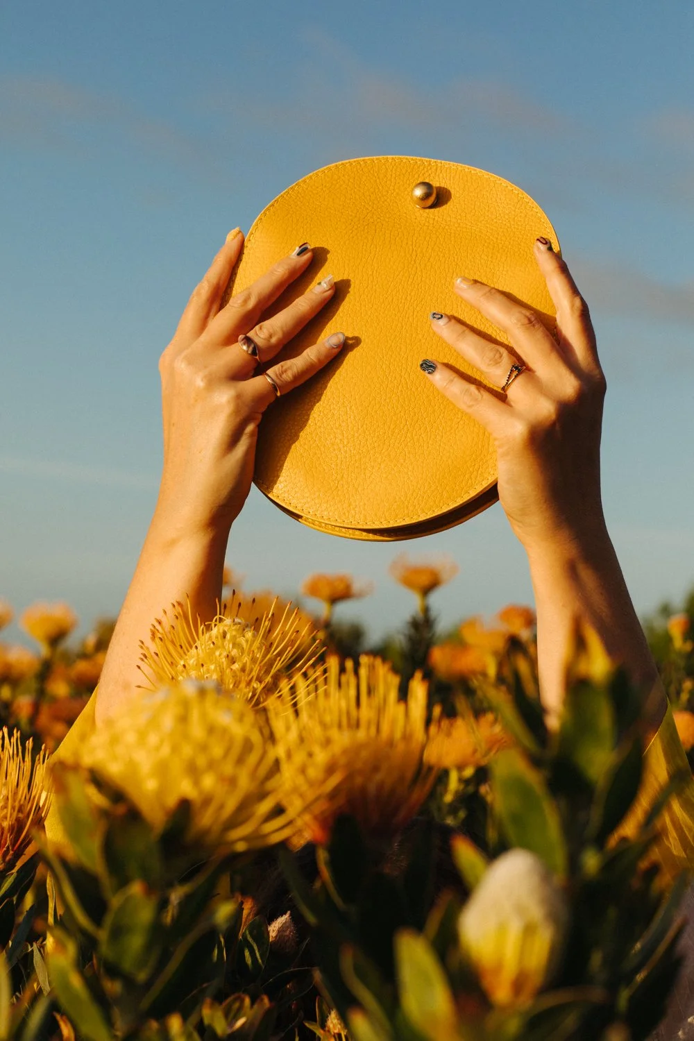 Beautiful still life image of hands holding a yellow leather bag against a blue sky. Fashion photography