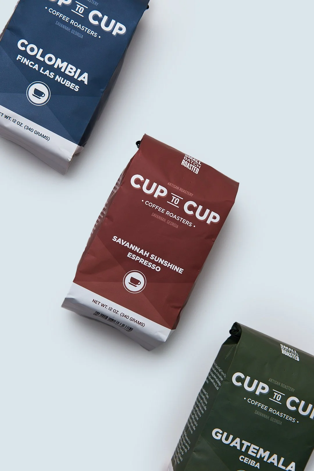 Three bags of coffee from Cup To Cup Coffee Roasters, featuring Colombian, Savannah Sunshine Espresso, and Guatemalan varieties, on a white surface.