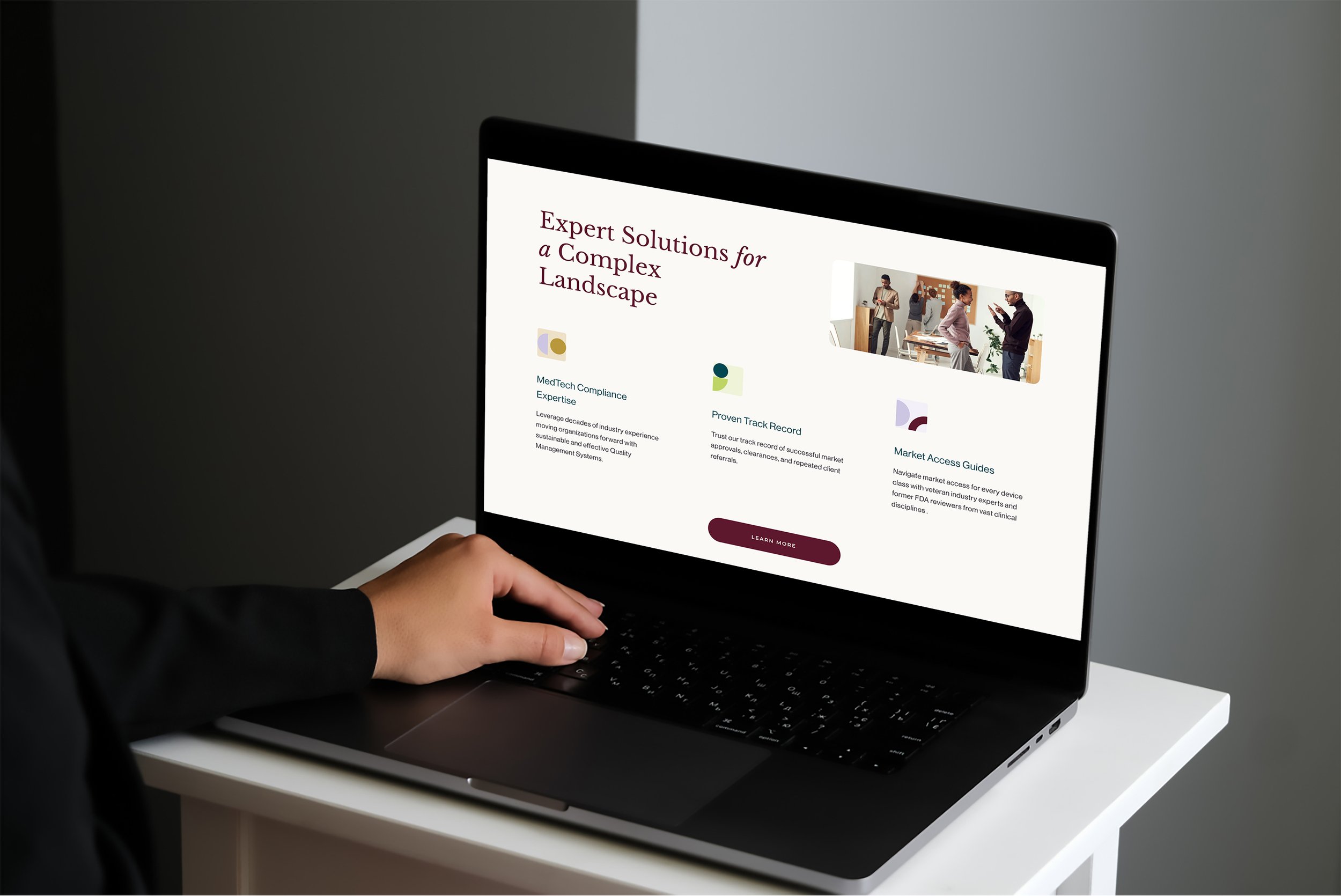 Person using a laptop on a white desk displaying a webpage about expert solutions for complex landscapes with text and images