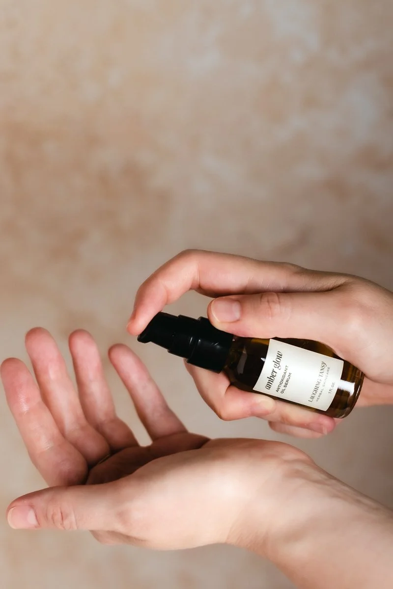 A person spraying a liquid from a dark amber bottle labeled 'Glow' onto their palm.
