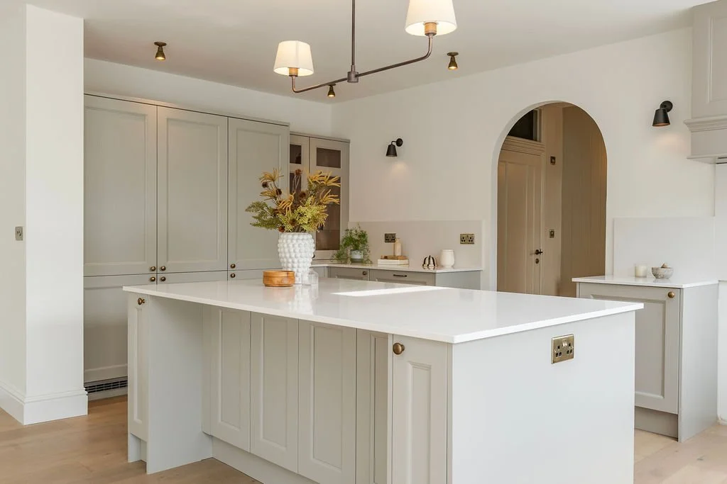 Modern kitchen with white cabinets and island, decorated with a vase of flowers, and featuring pendant and wall-mounted lights. Sophie Chapman, BIID Registered Interior Designer with 10 years experience. 30 Under 30 Cornwall 2022. Qualified