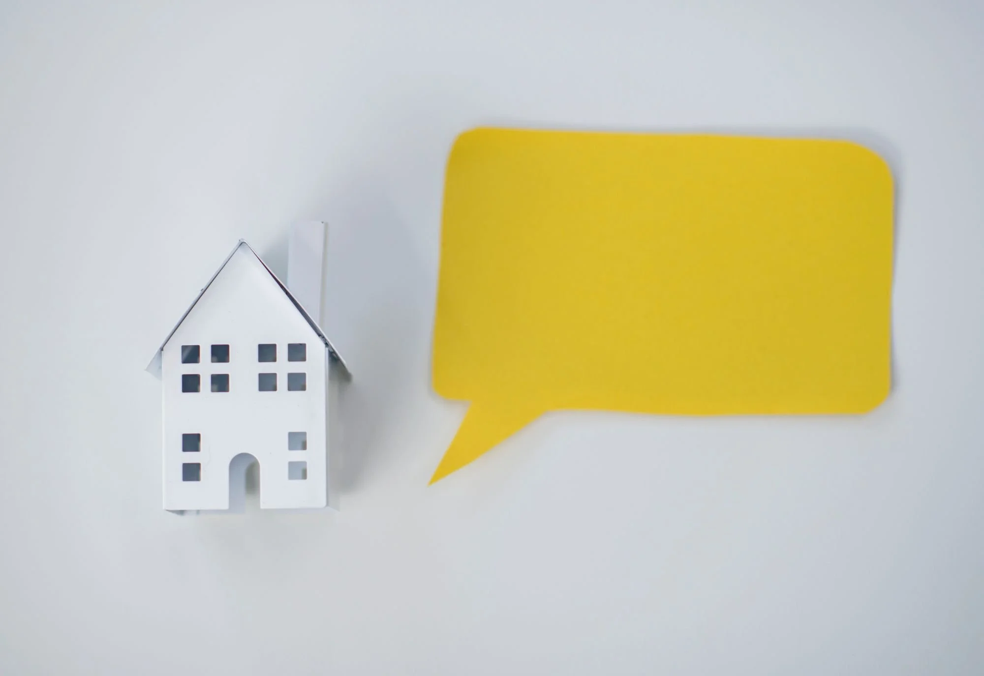 Miniature house model with yellow speech bubble on white background