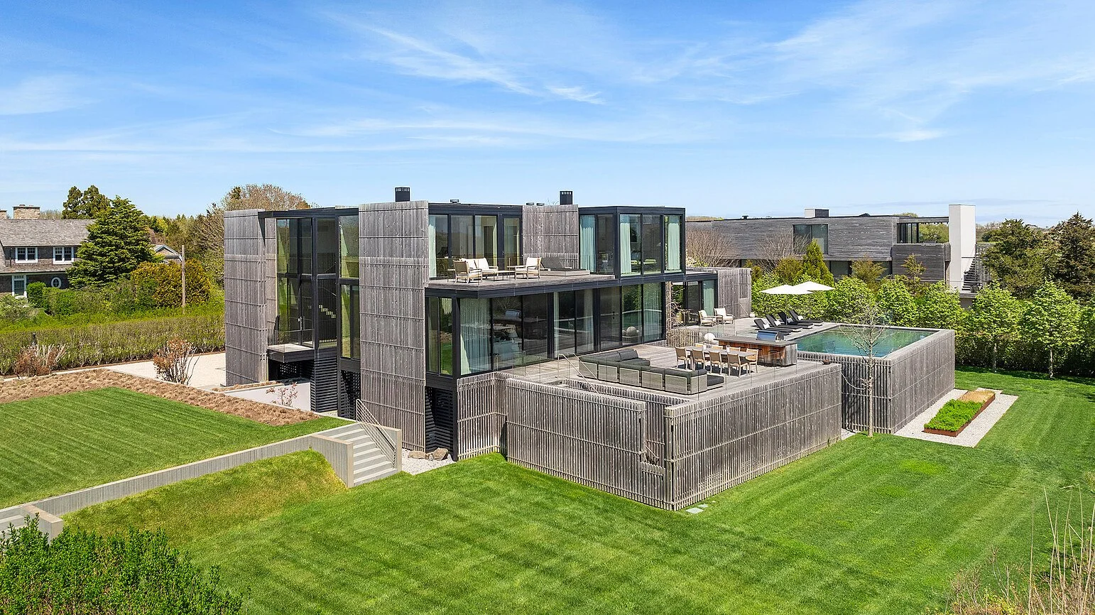 Drone view of a cedar-clad modern Hamptons home with pool and outdoor dining terrace