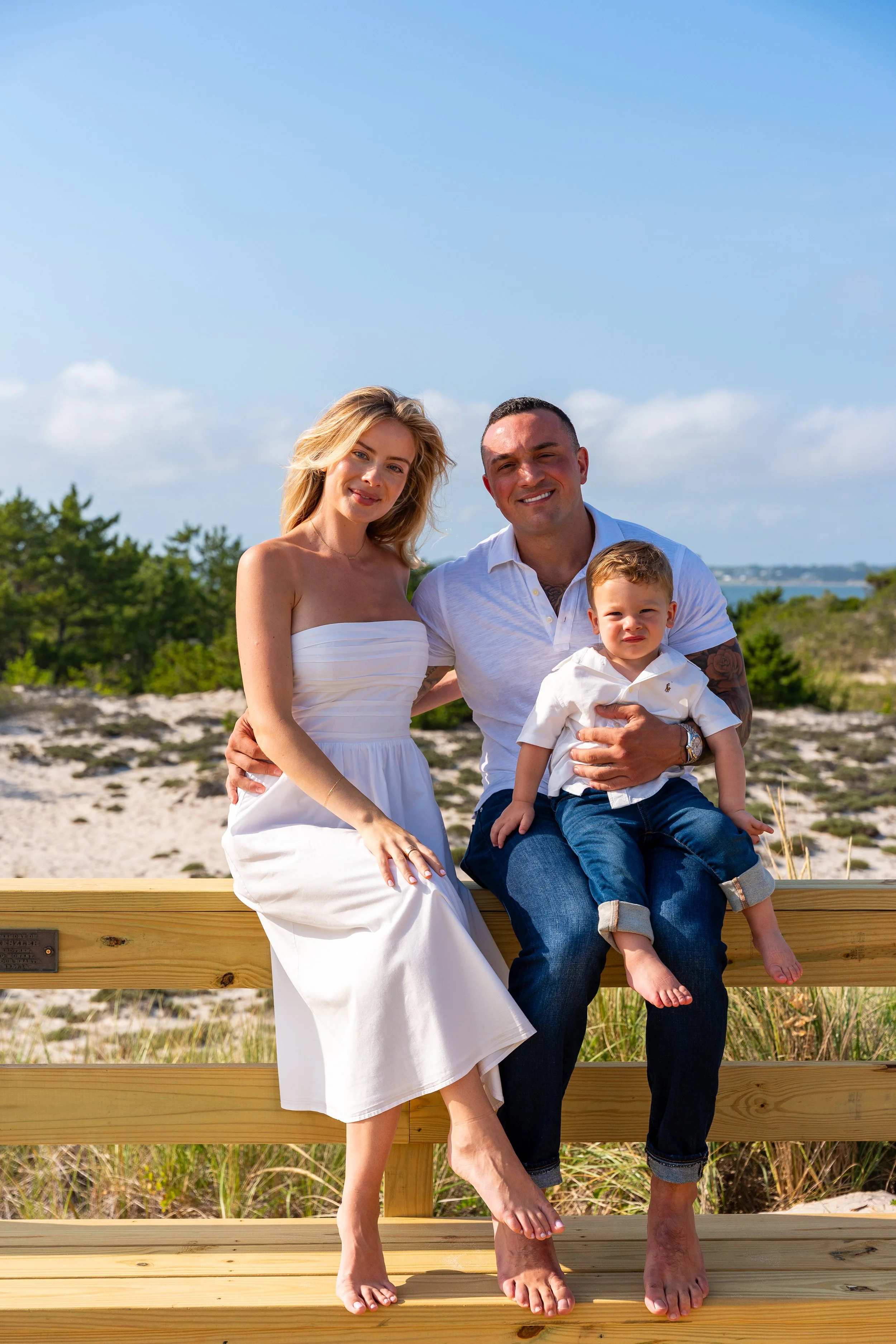Family of three sitting on a wooden fence by the beach dunes in the Hamptons