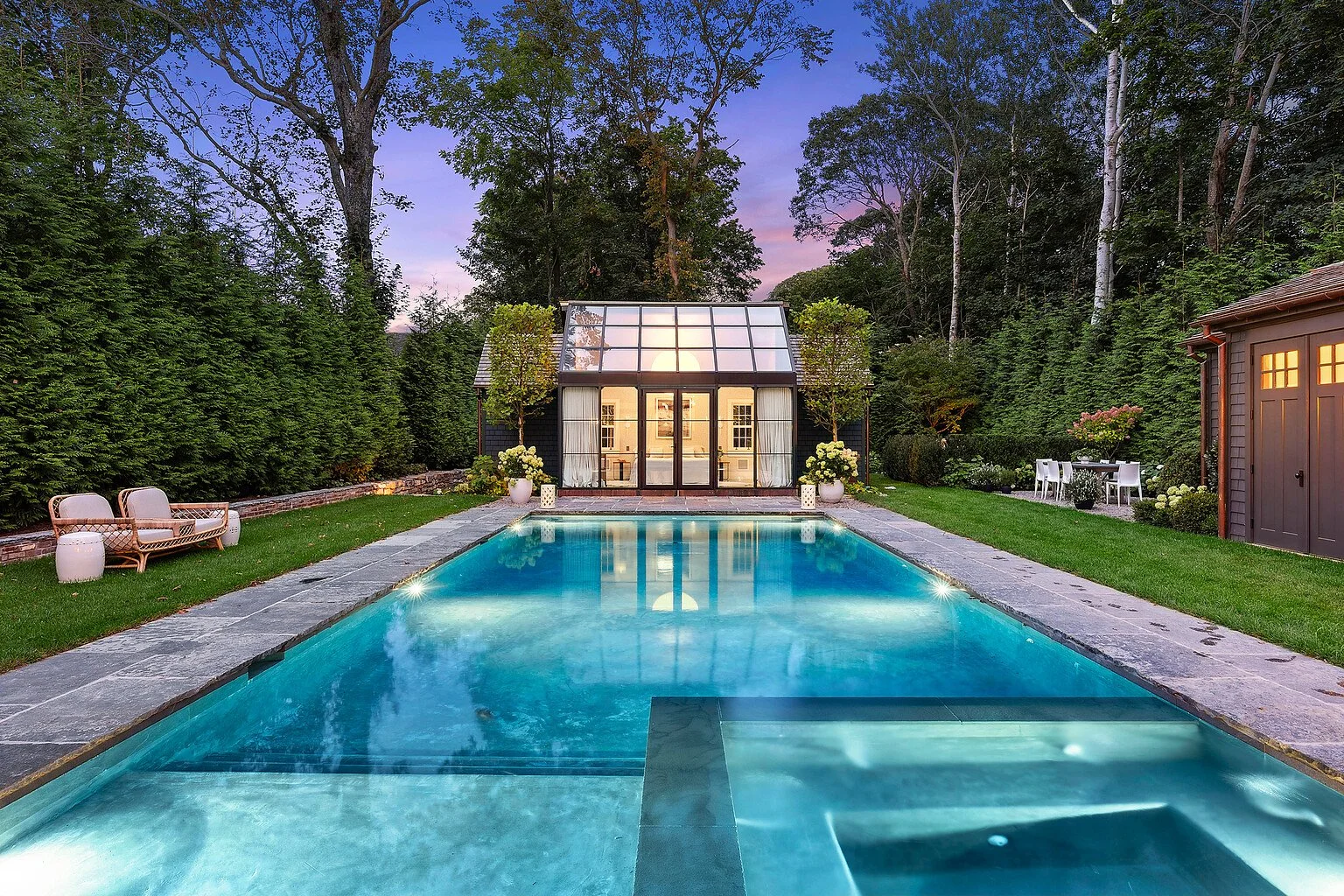 Heated pool and glass pool house at dusk in a Hamptons backyard