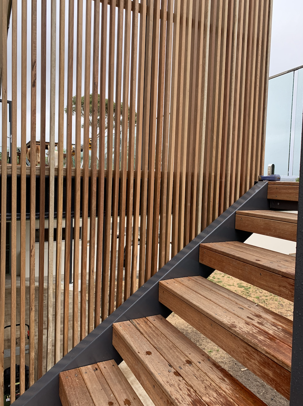 Wooden staircase with steps and a vertical wooden slat privacy screen outside.