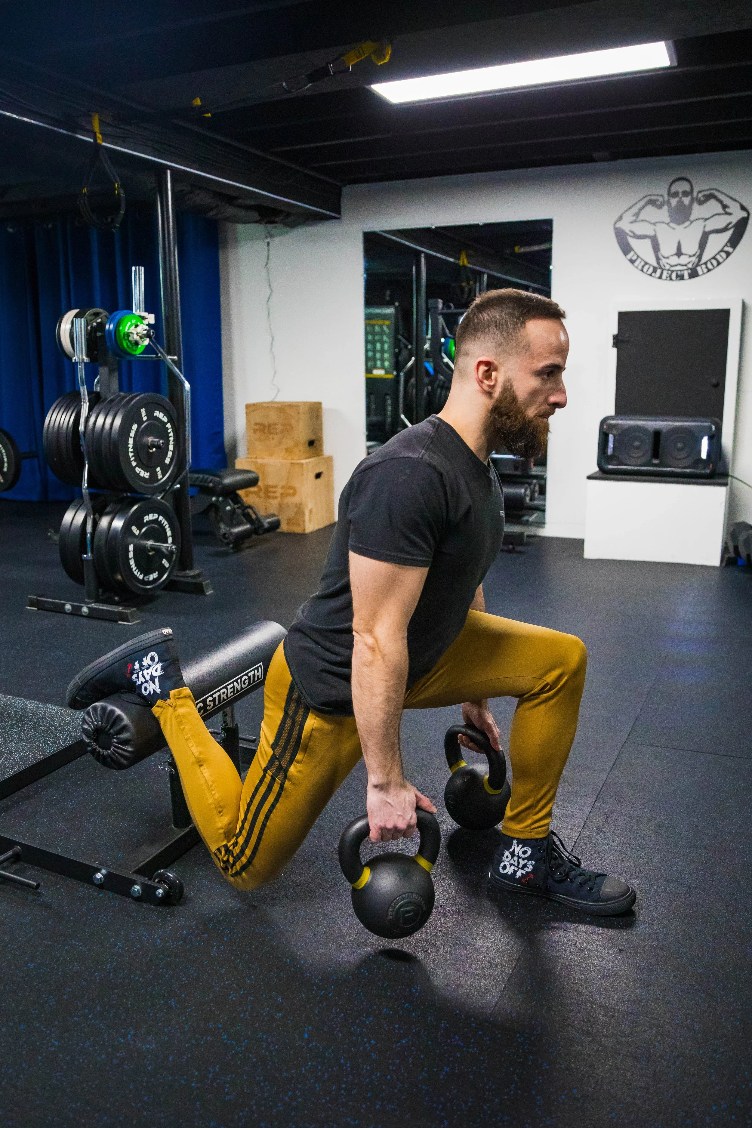 A man performing a lunge exercise with kettlebells in a gym.