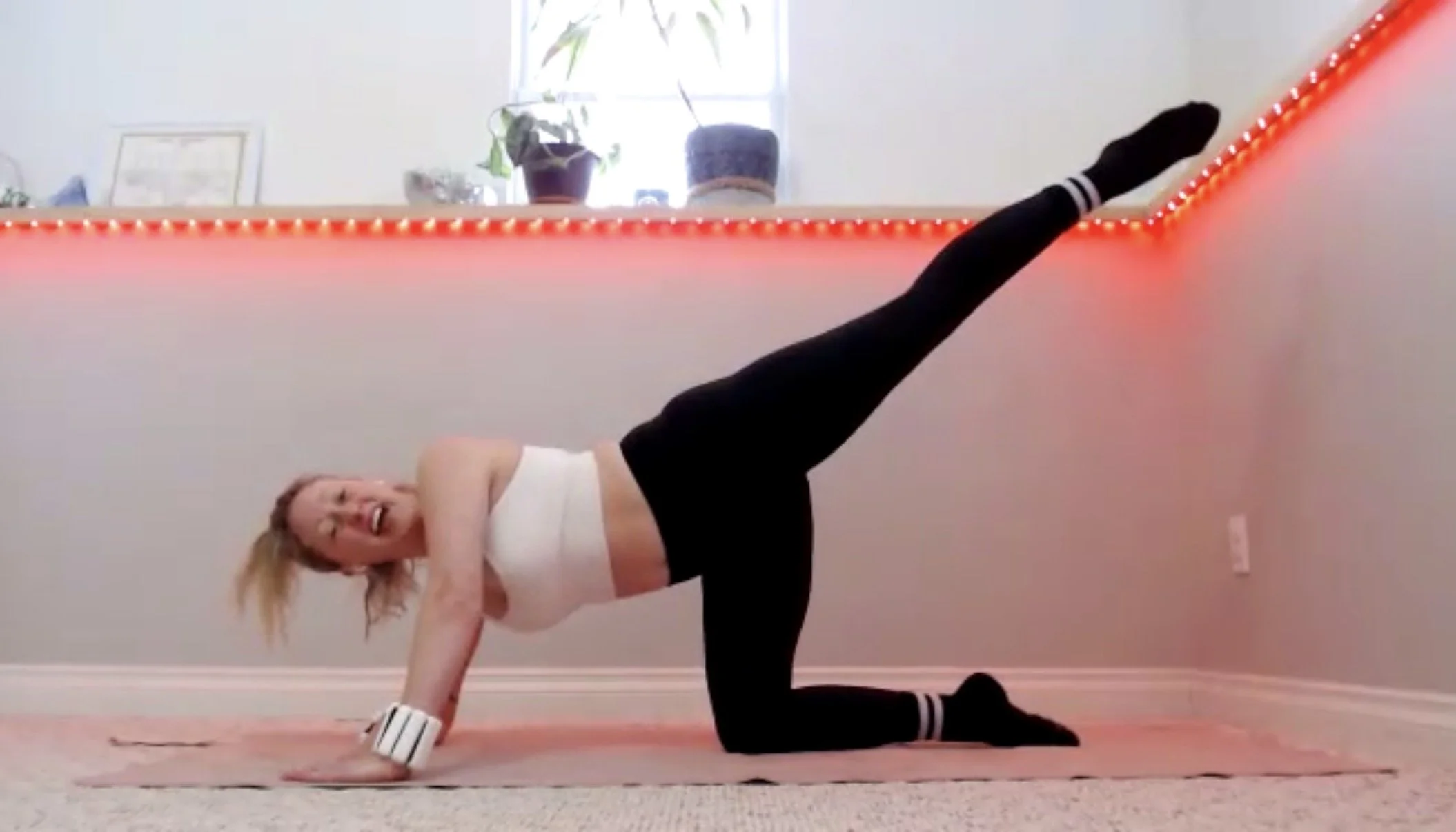 Woman doing yoga on beige carpet in front of decorated wall with holiday-themed decorations and a sign that says 'HAPPY HOLIDAYS'.