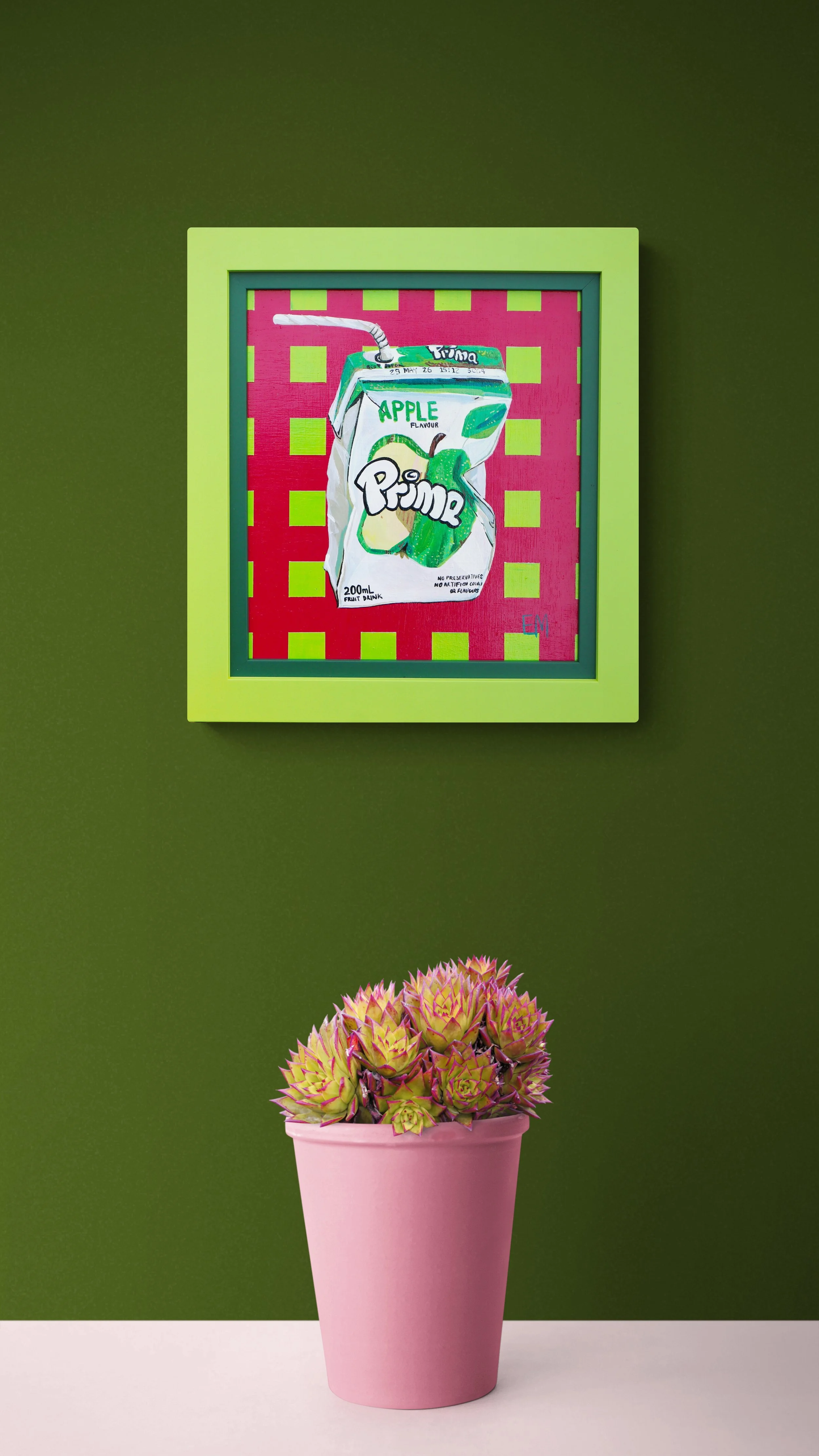 A potted succulent plant with pink and green leaves in a pink vase, placed against a green wall. Above, a framed artwork of a juice box with a straw on a pink background.