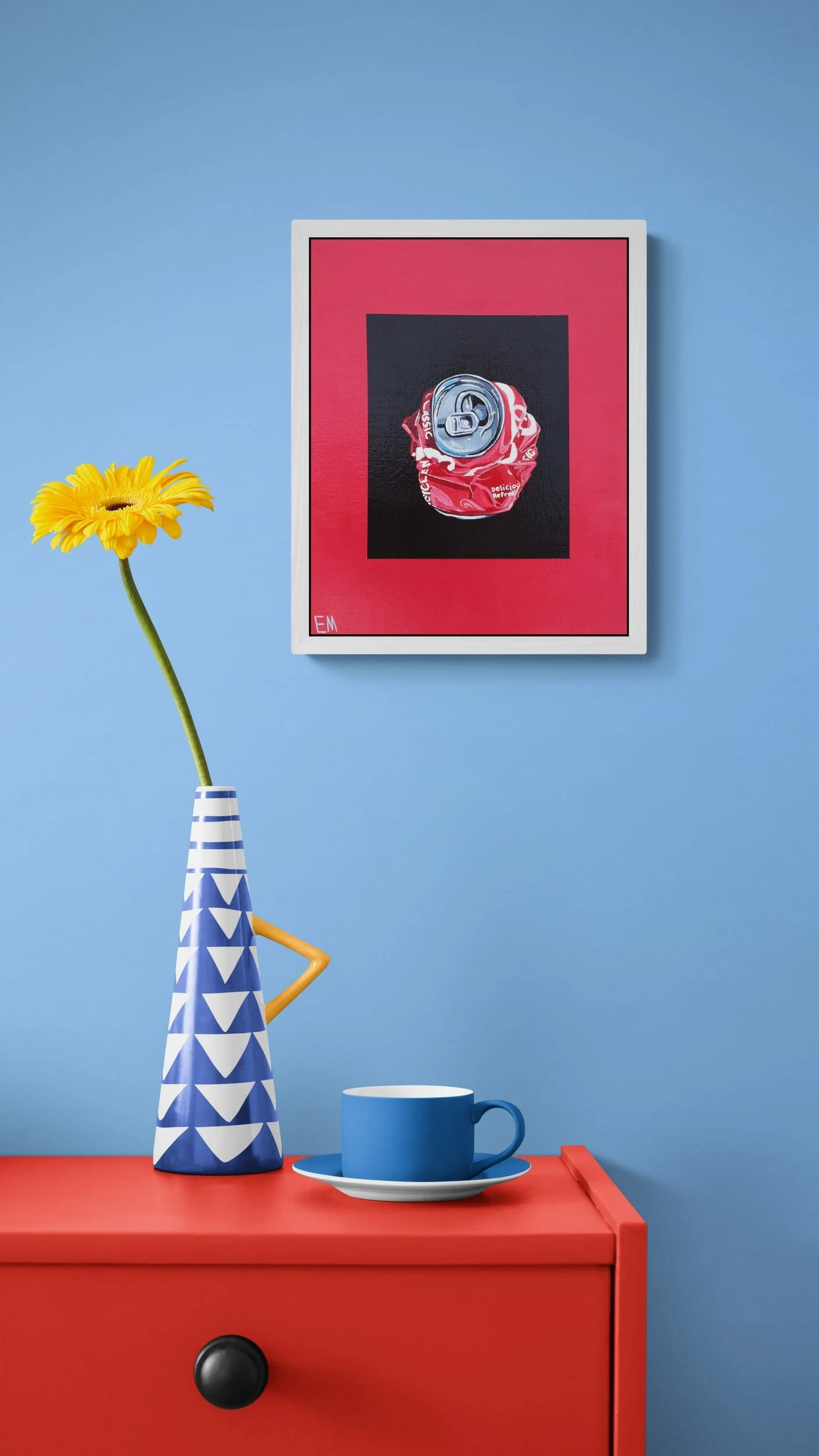 red and black cola can crushed framed in white hangs on blue wall