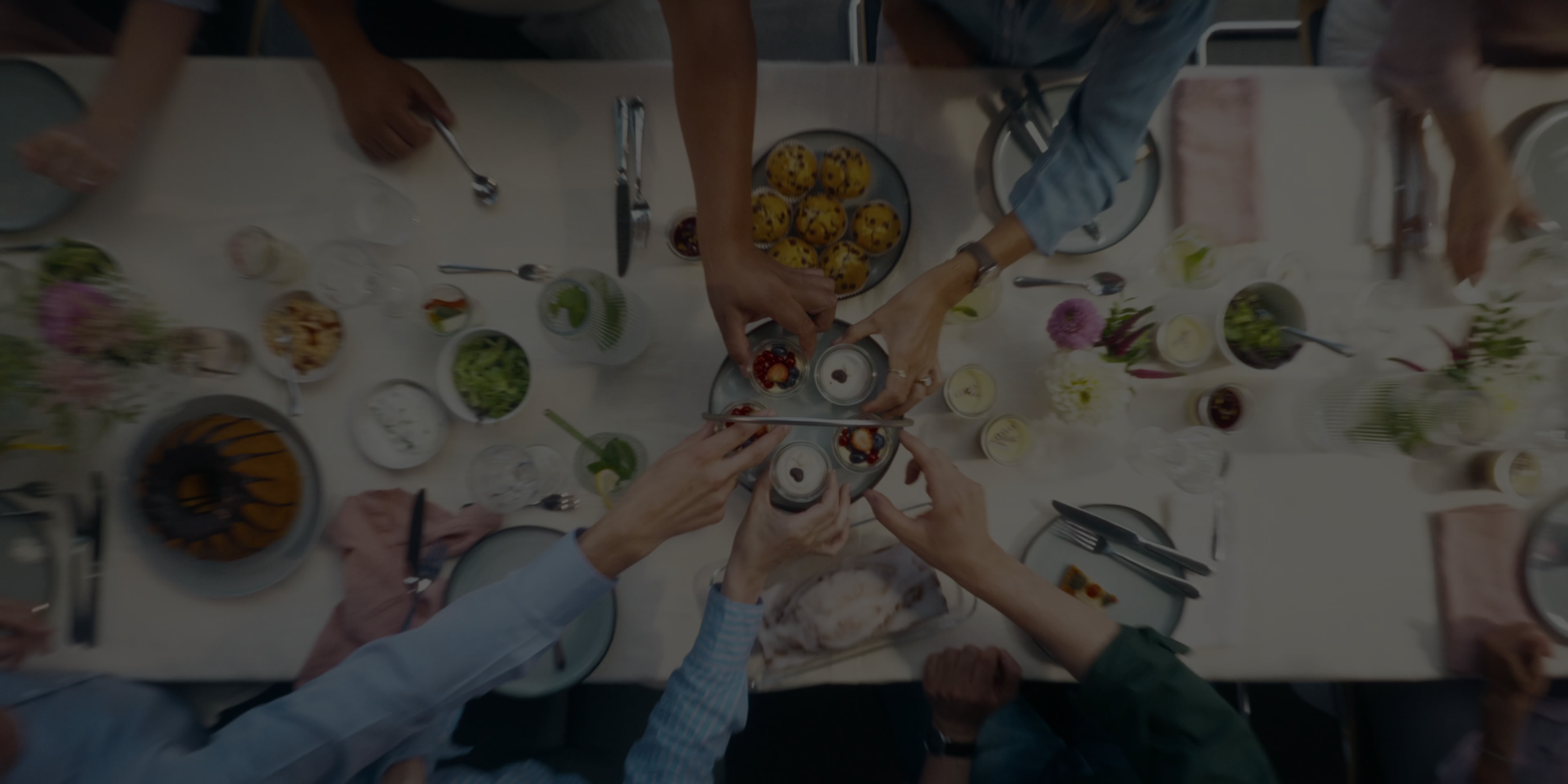 People gathered around a table celebrating, clinking dessert glasses topped with whipped cream and berries.