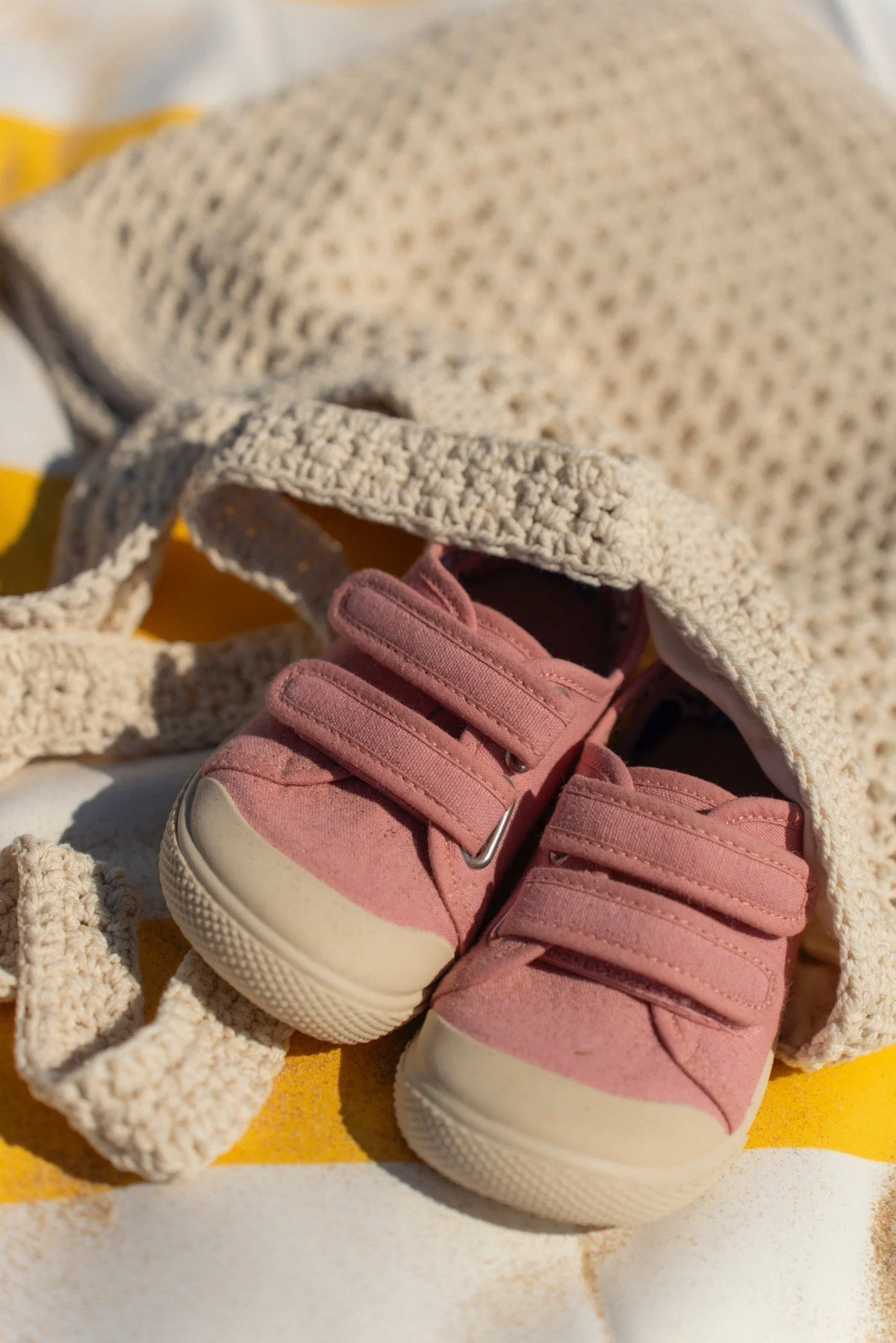 Un par de zapatitos rosados con velcro descansando sobre un cartón amarillo, con un saco de punto cremoso a su alrededor.