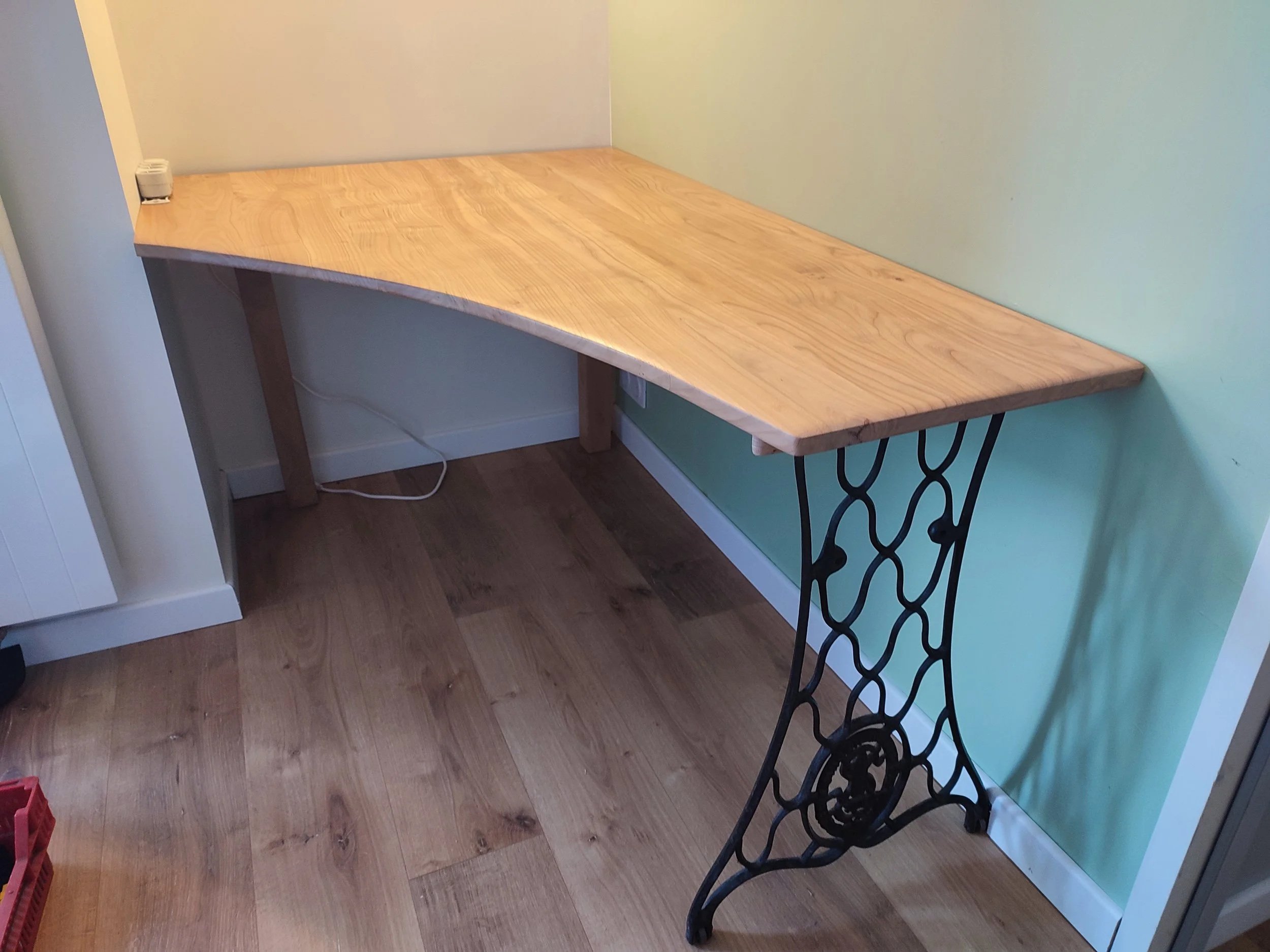 Une salle avec un mur blanc, une grande étagère en bois avec des supports en métal noir, une porte-fenêtre donnant sur un espace extérieur avec des arbres et une chaise bleue, un meuble en bois avec des tiroirs et des poignées noires.