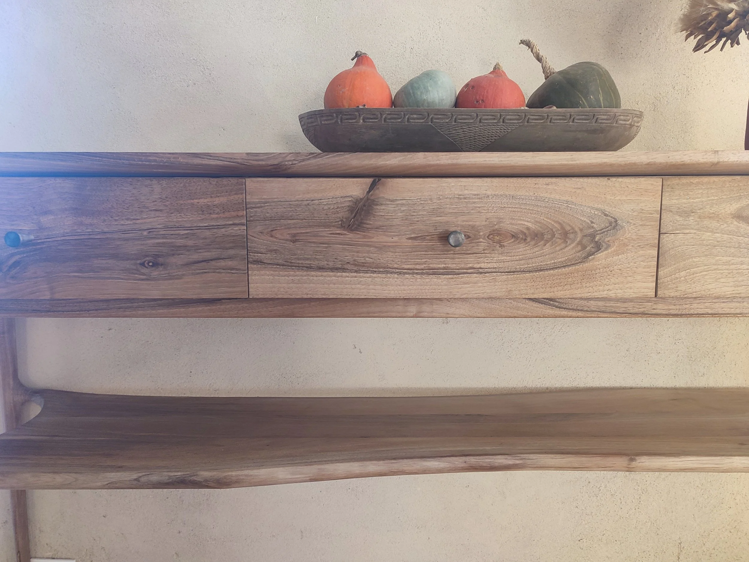 Étagère en bois clair avec supports noirs fixée à un mur blanc dans une pièce lumineuse, avec une fenêtre ouverte laissant entrer la lumière naturelle.