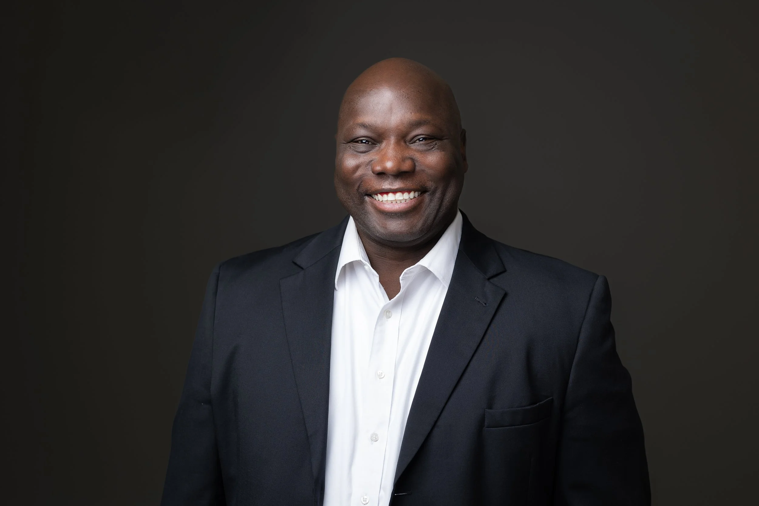 Portrait of a smiling African American man in a business suit against a dark background.