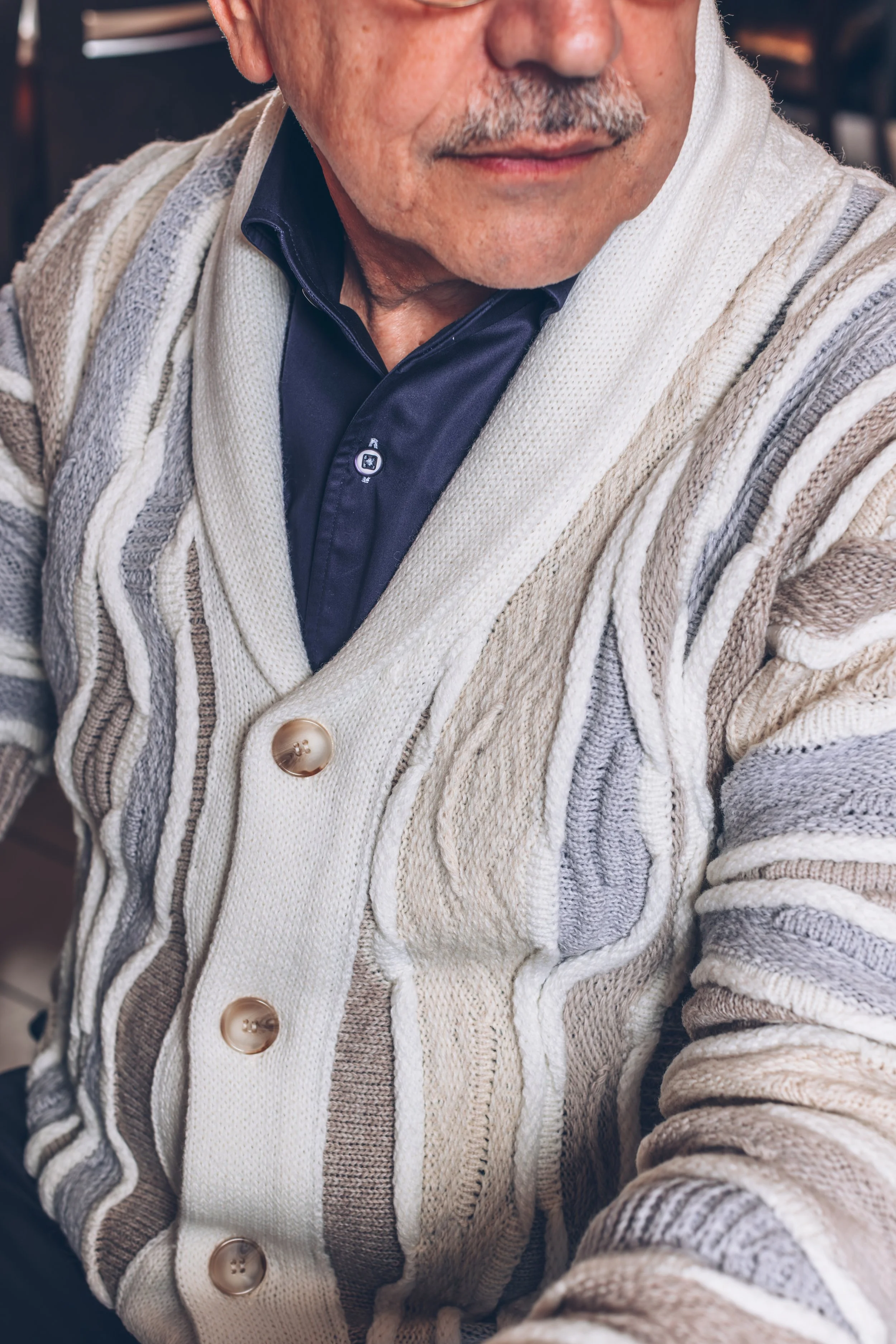 Close-up of a man wearing a patterned knit cardigan over a dark blue collared shirt, showing part of his face and chest.