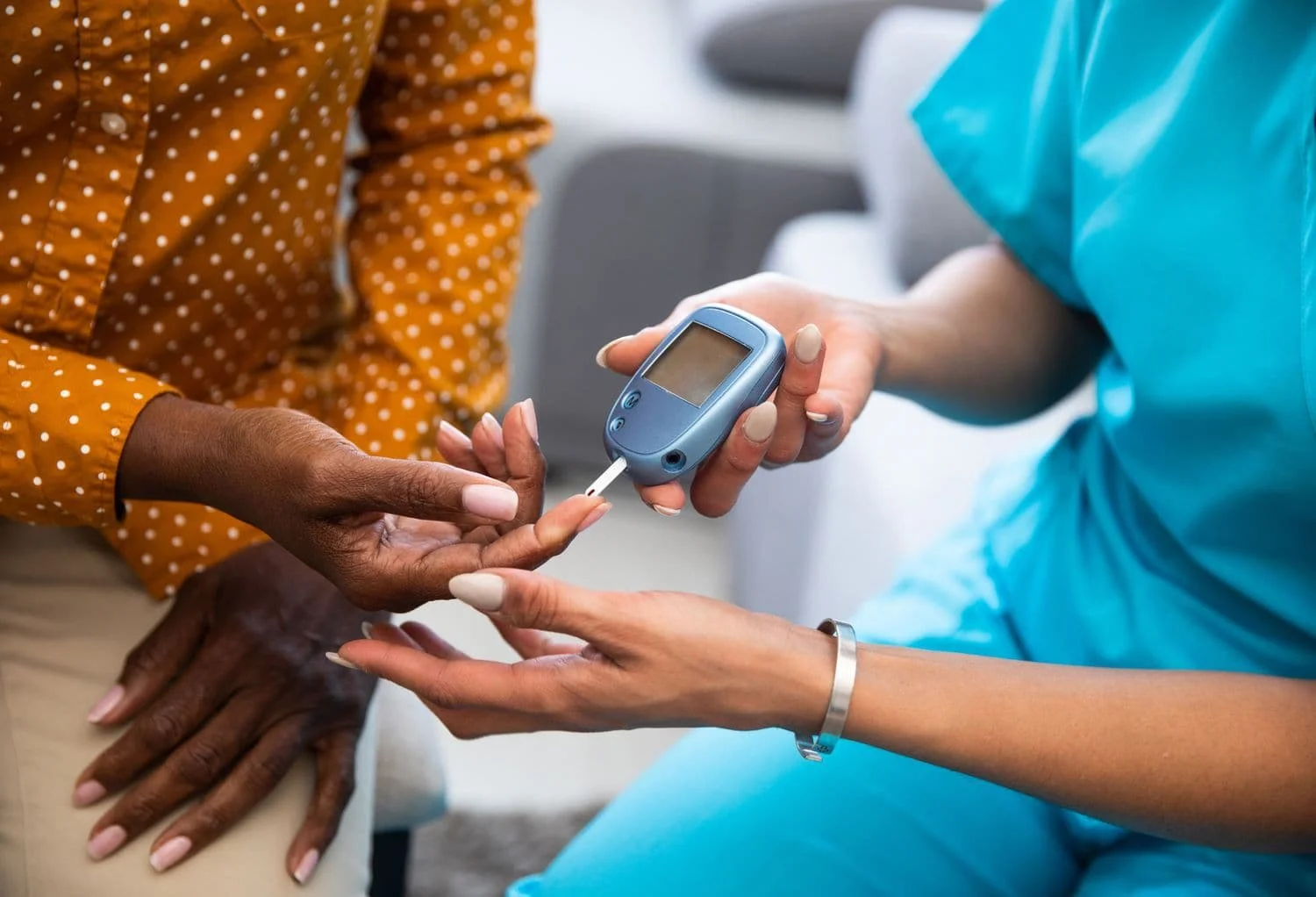 A person in medical scrubs using a blood glucose meter to check blood sugar levels of another person.