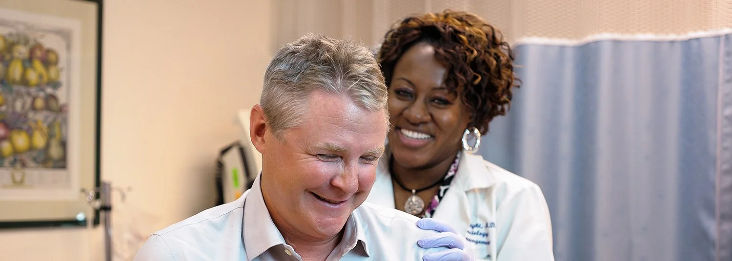 A healthcare professional, wearing gloves and a white coat, caring for a smiling man in a medical setting.