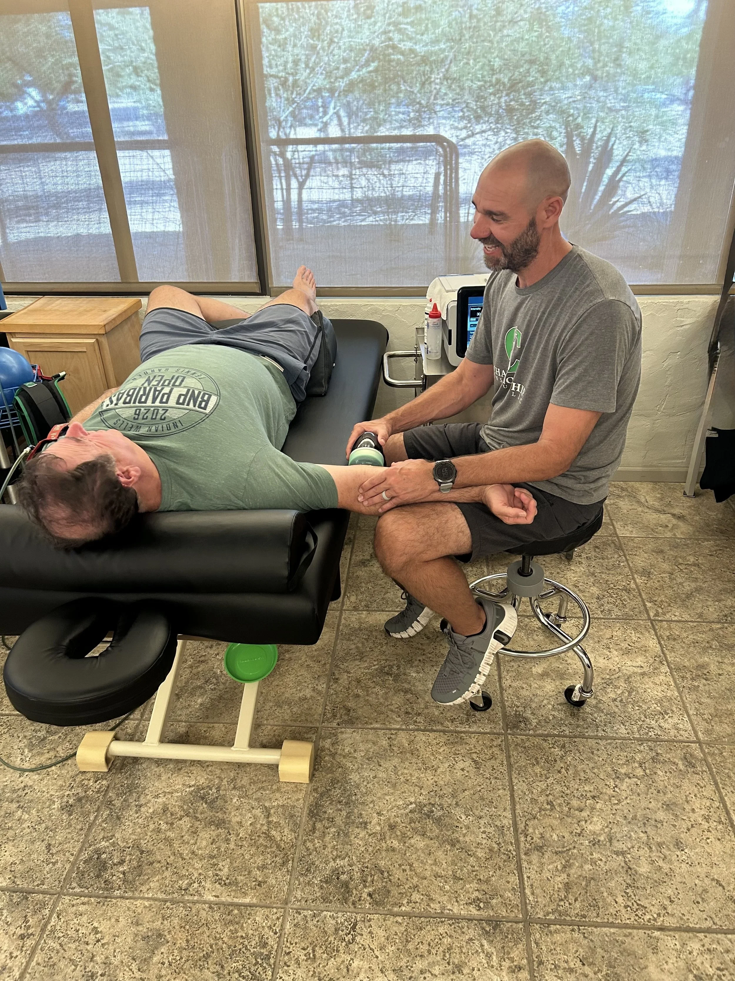 A man wearing a green shirt is lying getting shockwave therapy performed on an injury by Chris Murphy at Championship Institute, in Tucson Arizona
