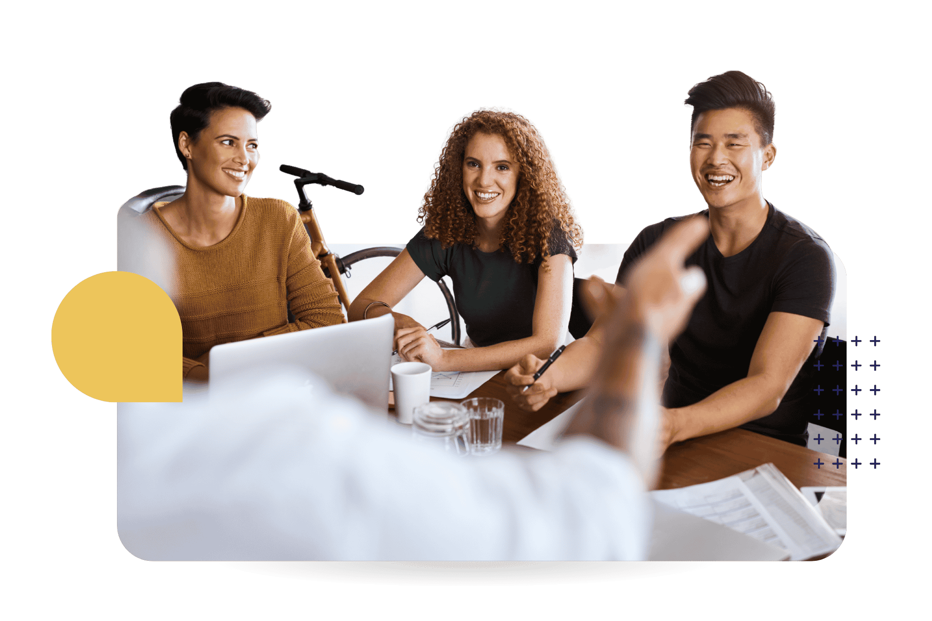 Three colleagues smiling and laughing during an in-person training session around a conference table.