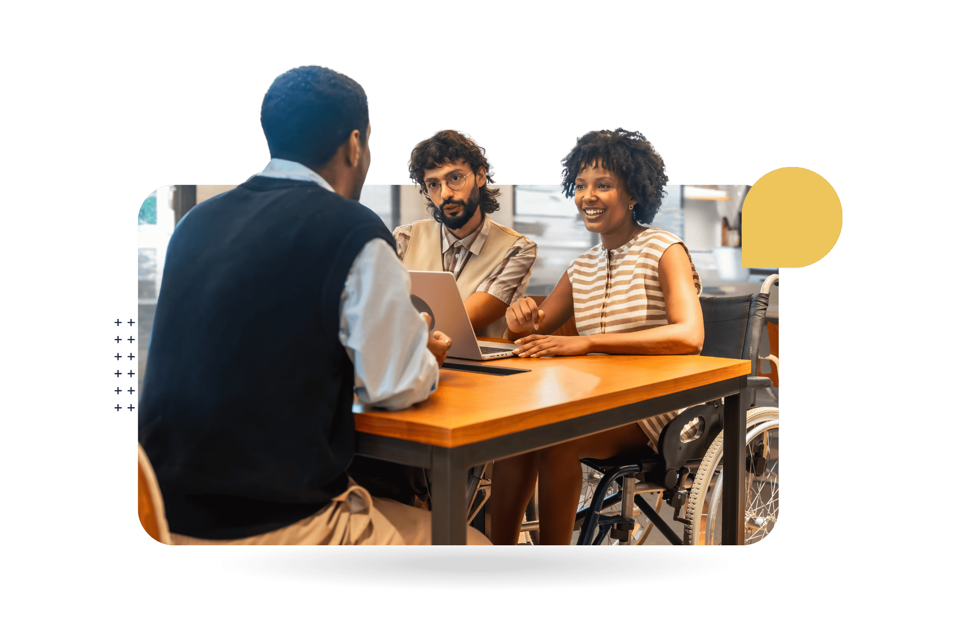 Three coworkers sit around a table in a modern office during a collaborative meeting. One participant is using a wheelchair, highlighting workplace inclusion and accessibility.