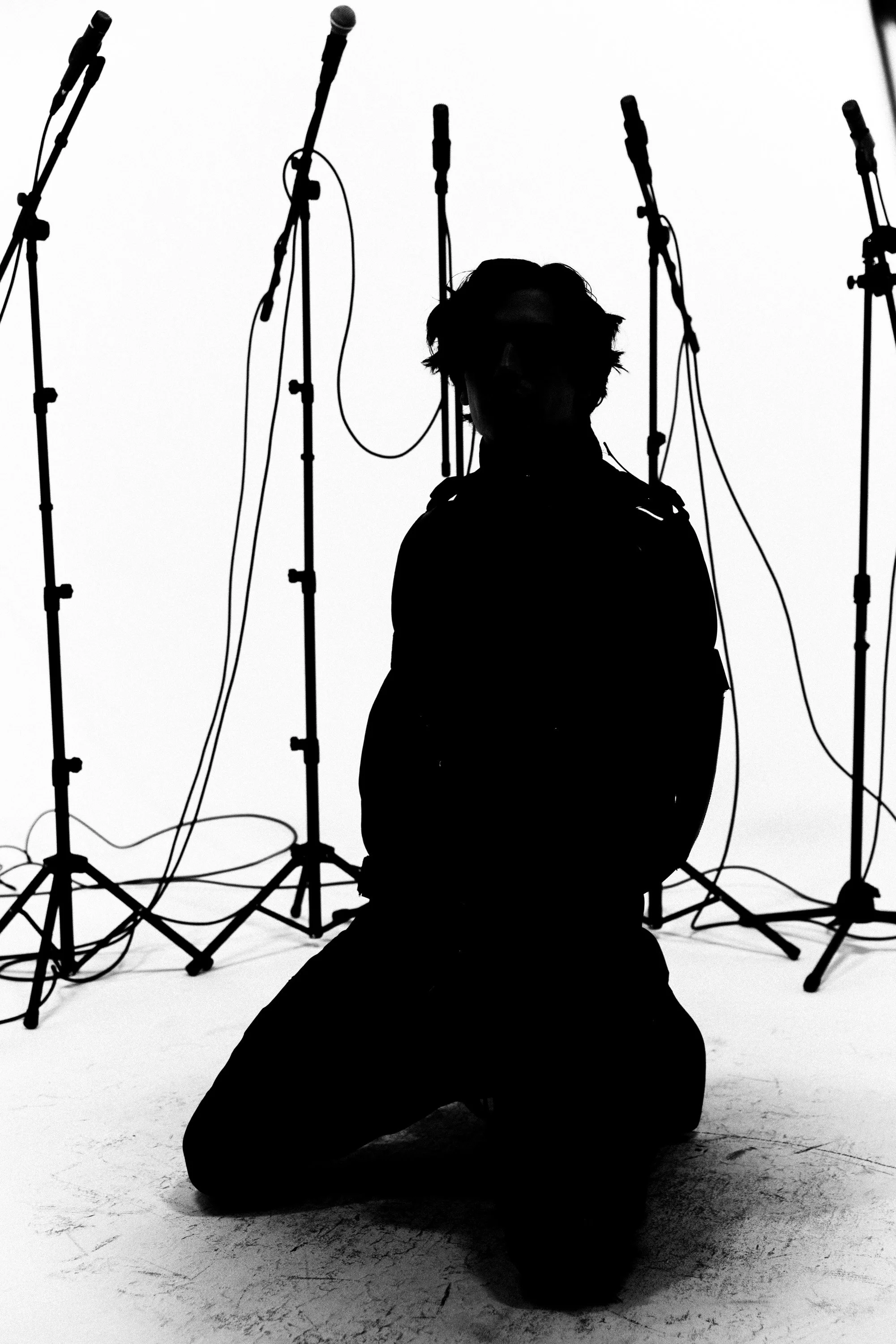 A person in silhouette kneeling with microphones on stands behind them in a studio setting.