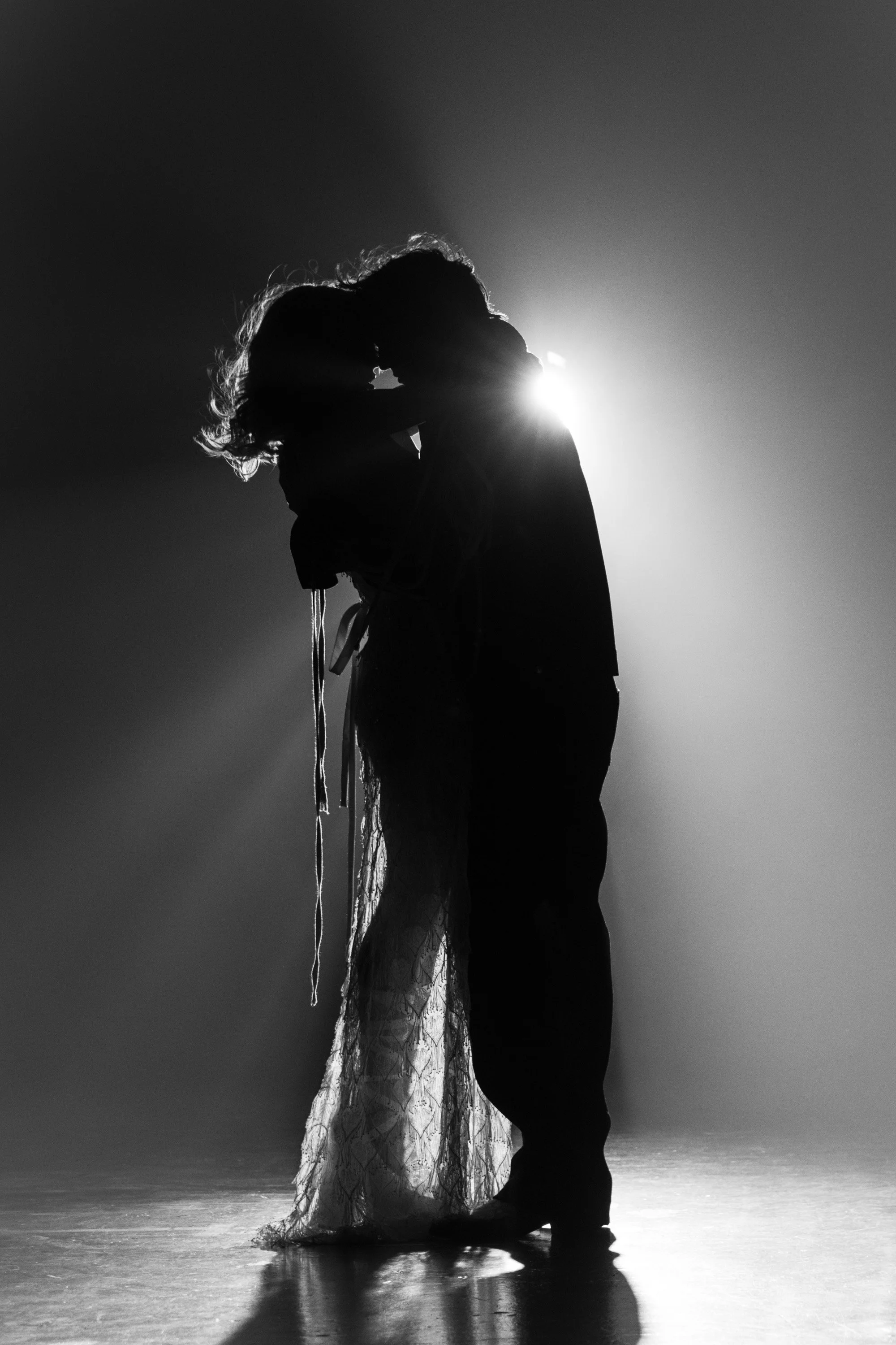 Silhouetted couple dancing closely on a stage with bright backlighting creating a halo effect around them.