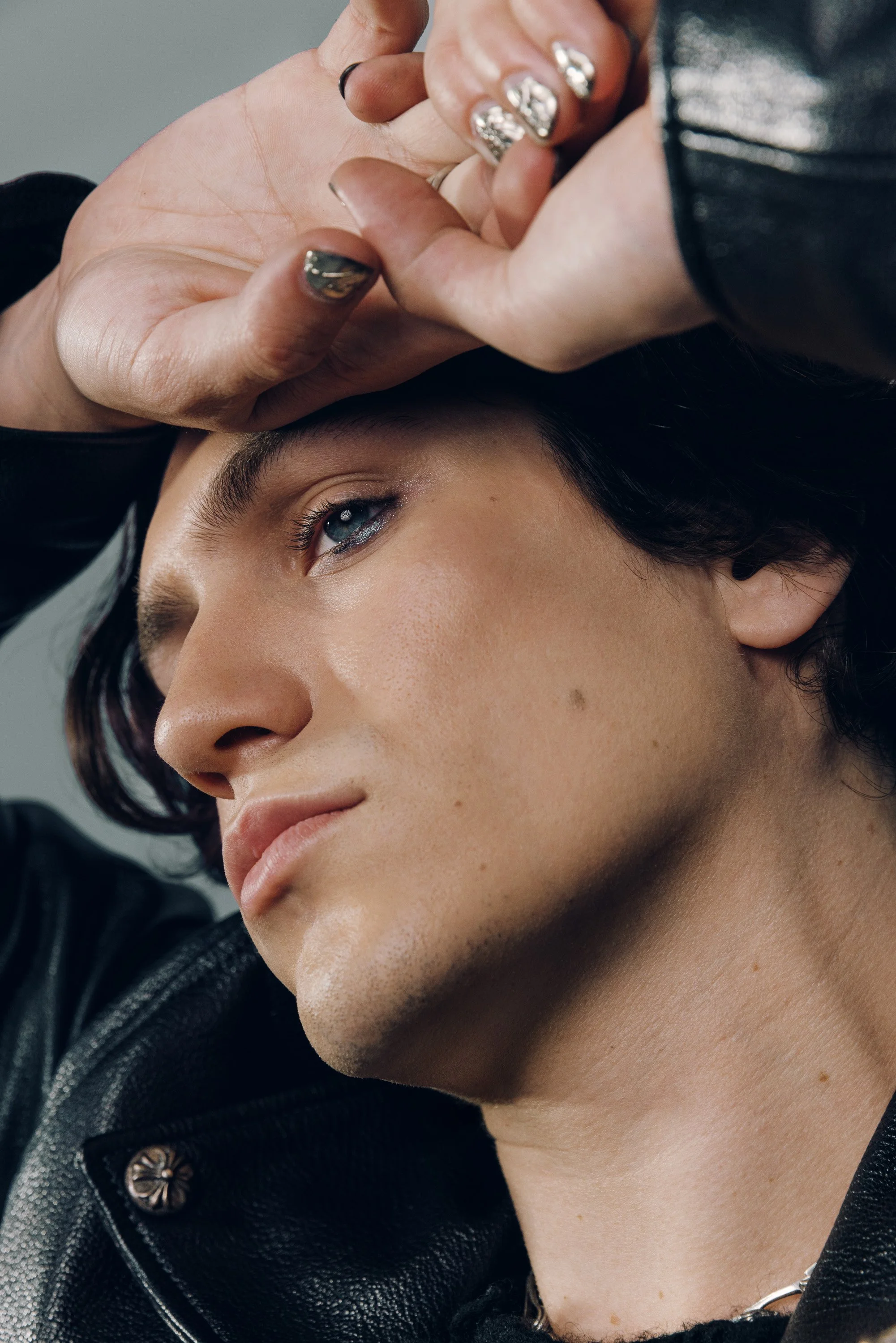 Close-up of a woman with dark hair lying back as a person with painted nails holds her forehead. The woman has blue eyes and smooth skin.