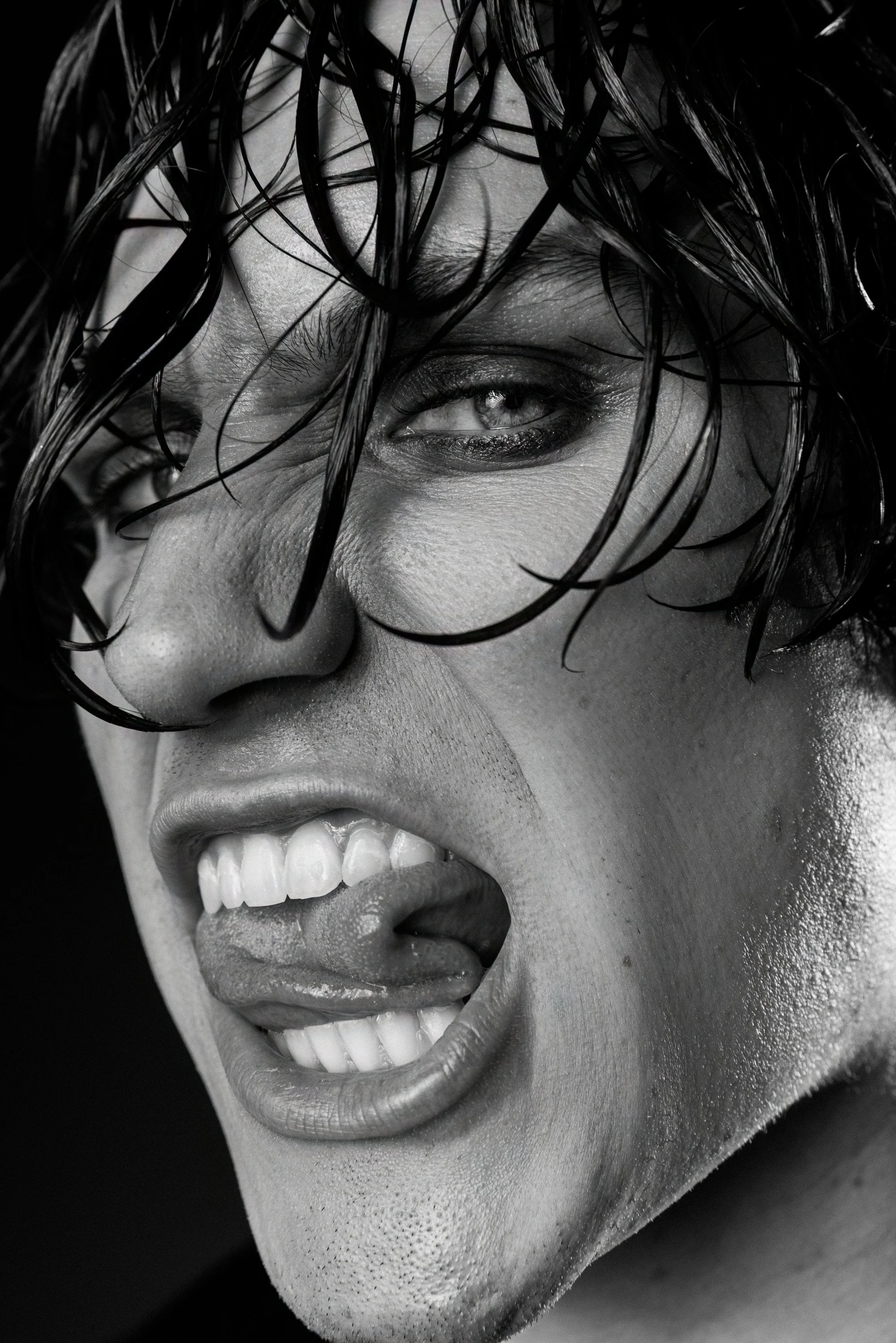 Close-up black and white photo of a smiling woman with wet hair covering part of her face.