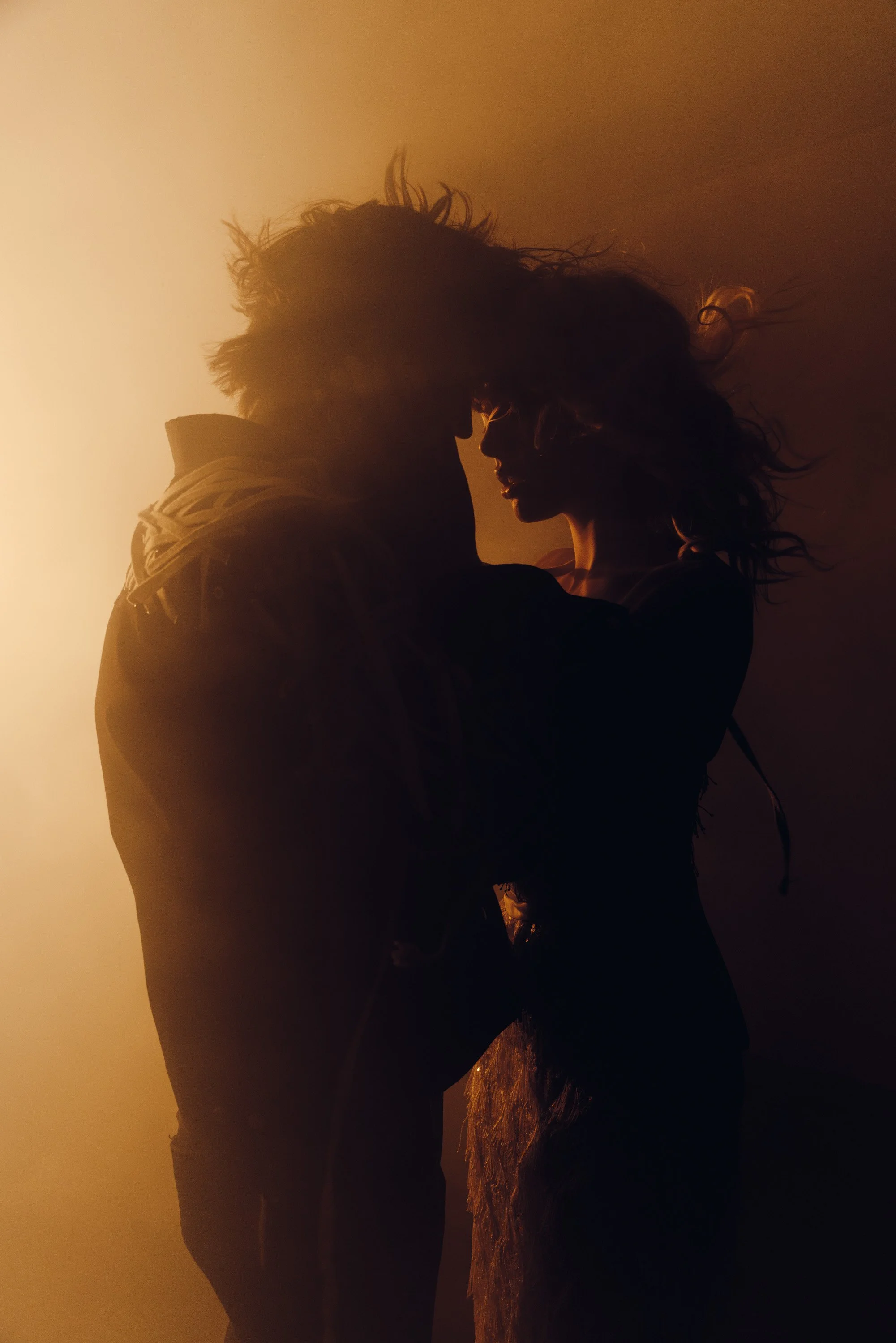 Silhouettes of a man and a woman close together at sunset, on rocky terrain.