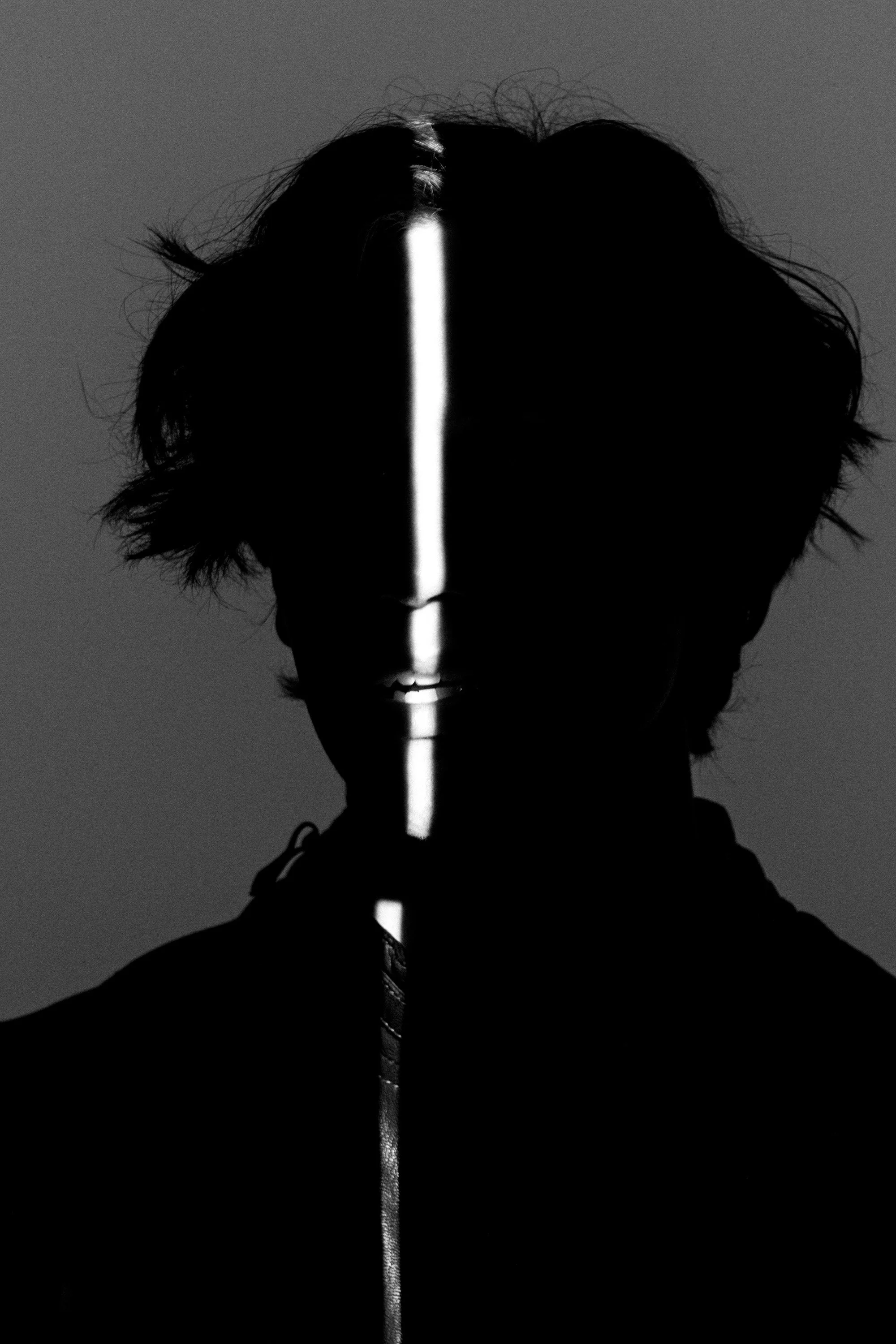 A person holding a luminous white stick vertically with a triangular top, silhouetted against a gray background, with their face partially obscured by shadows.