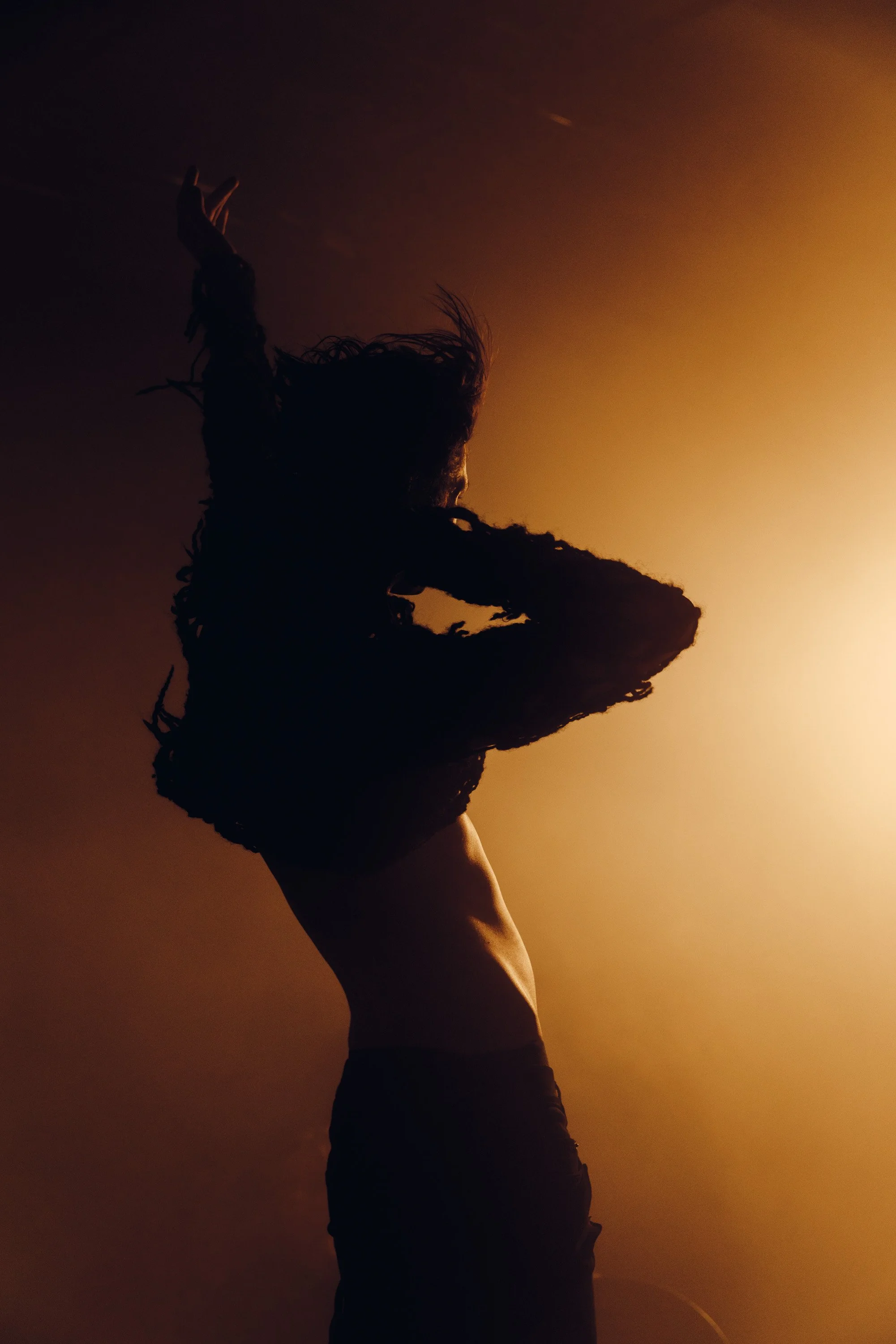 A silhouette of a woman with her arm raised against a warm, golden-orange gradient background.