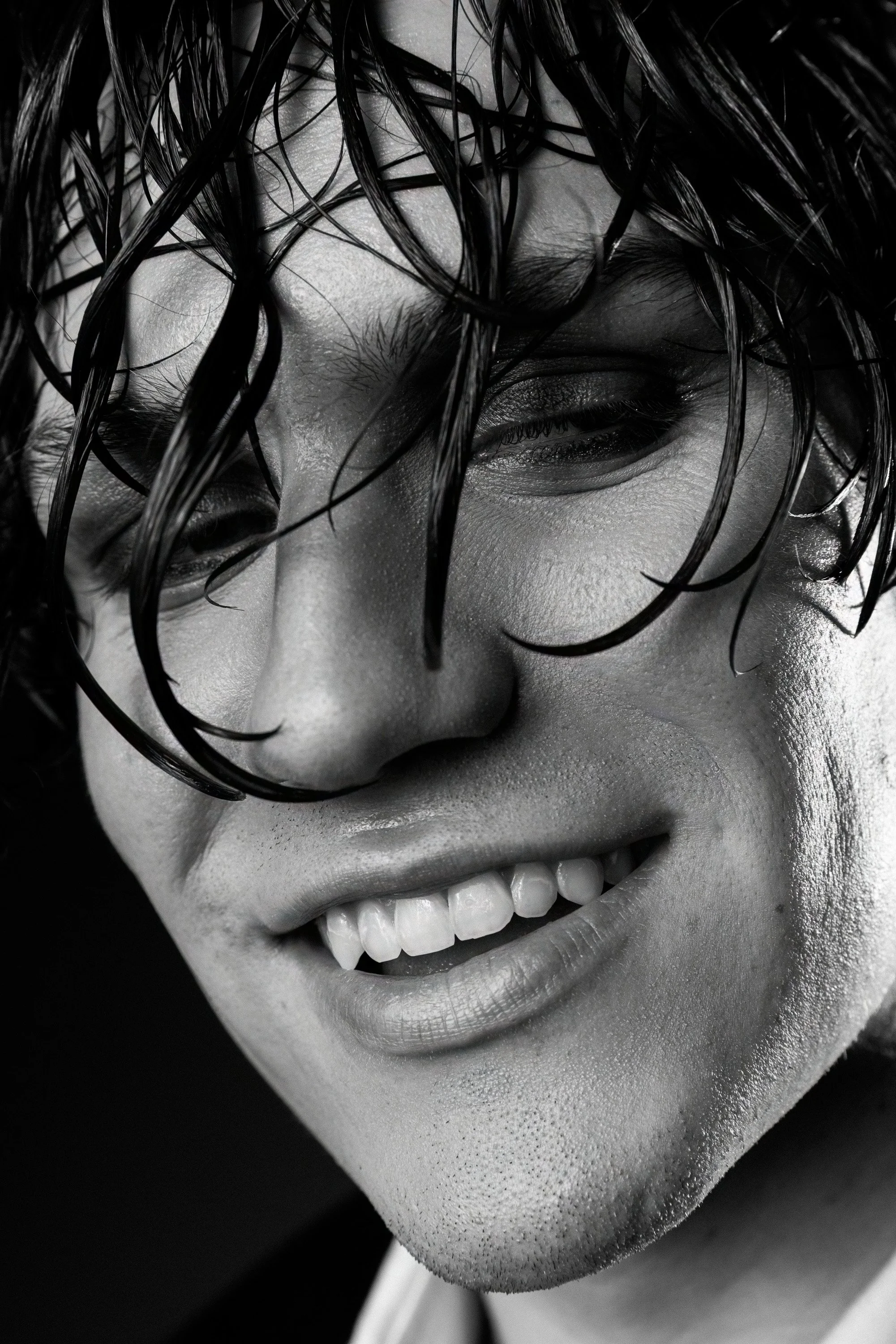 Close-up black and white photo of a smiling woman with wet, messy hair partially covering her face, showing her eyes, nose, and mouth.