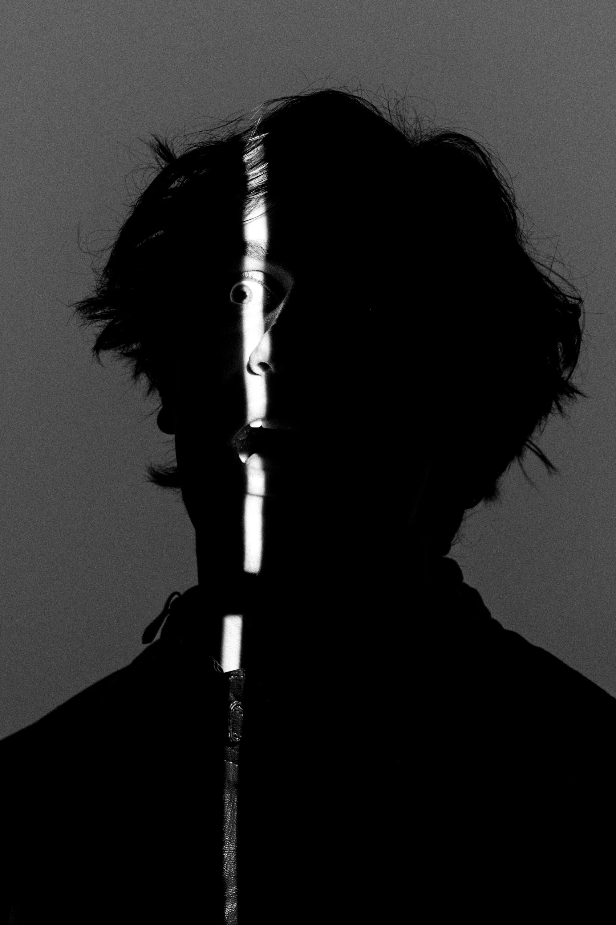 Black and white photo of a person with messy hair holding a flashlight vertically in front of their face, partially obscuring it.