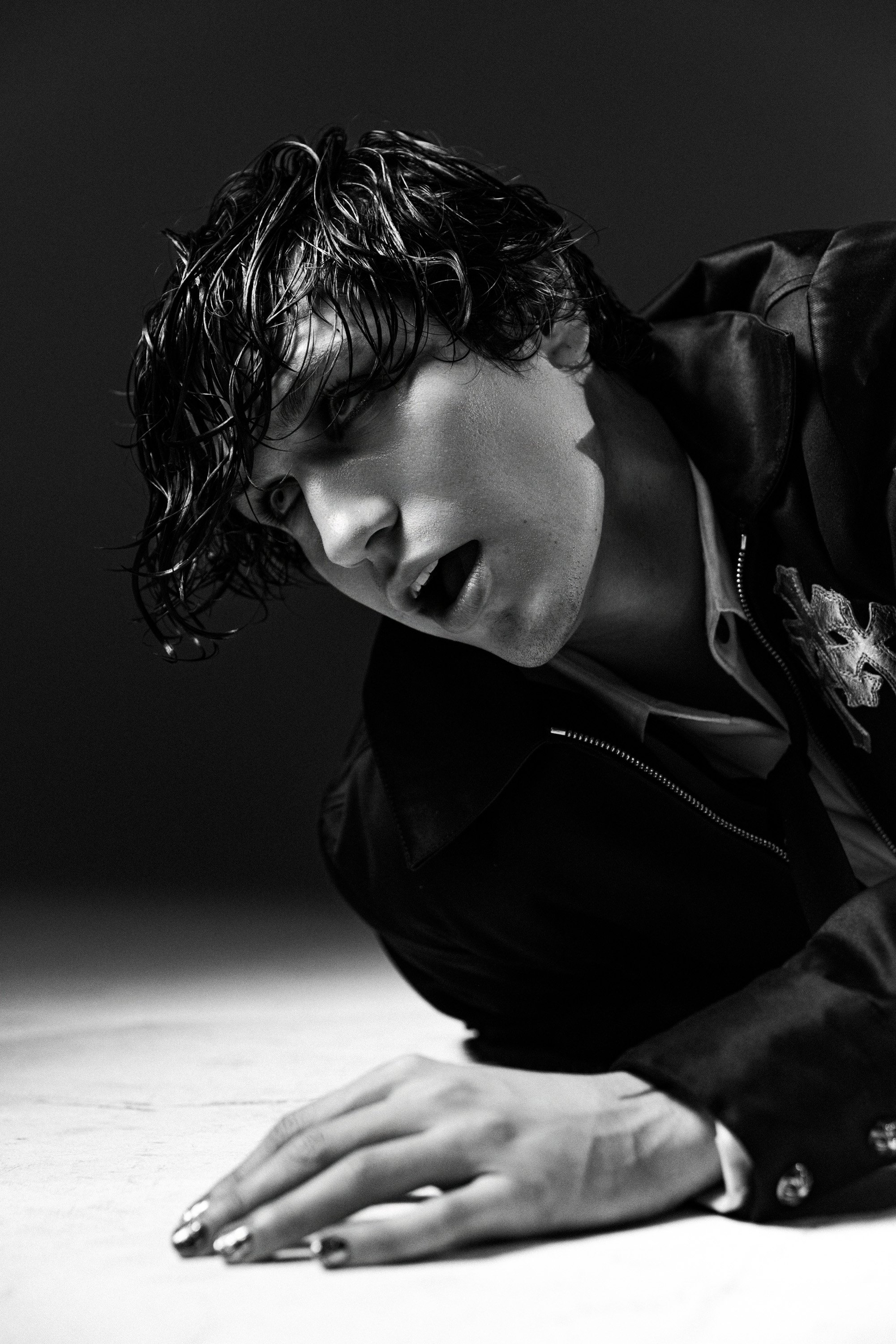 Black and white photo of a person with wet, curly hair, leaning forward, with their hands flat on a surface, wearing a leather jacket.