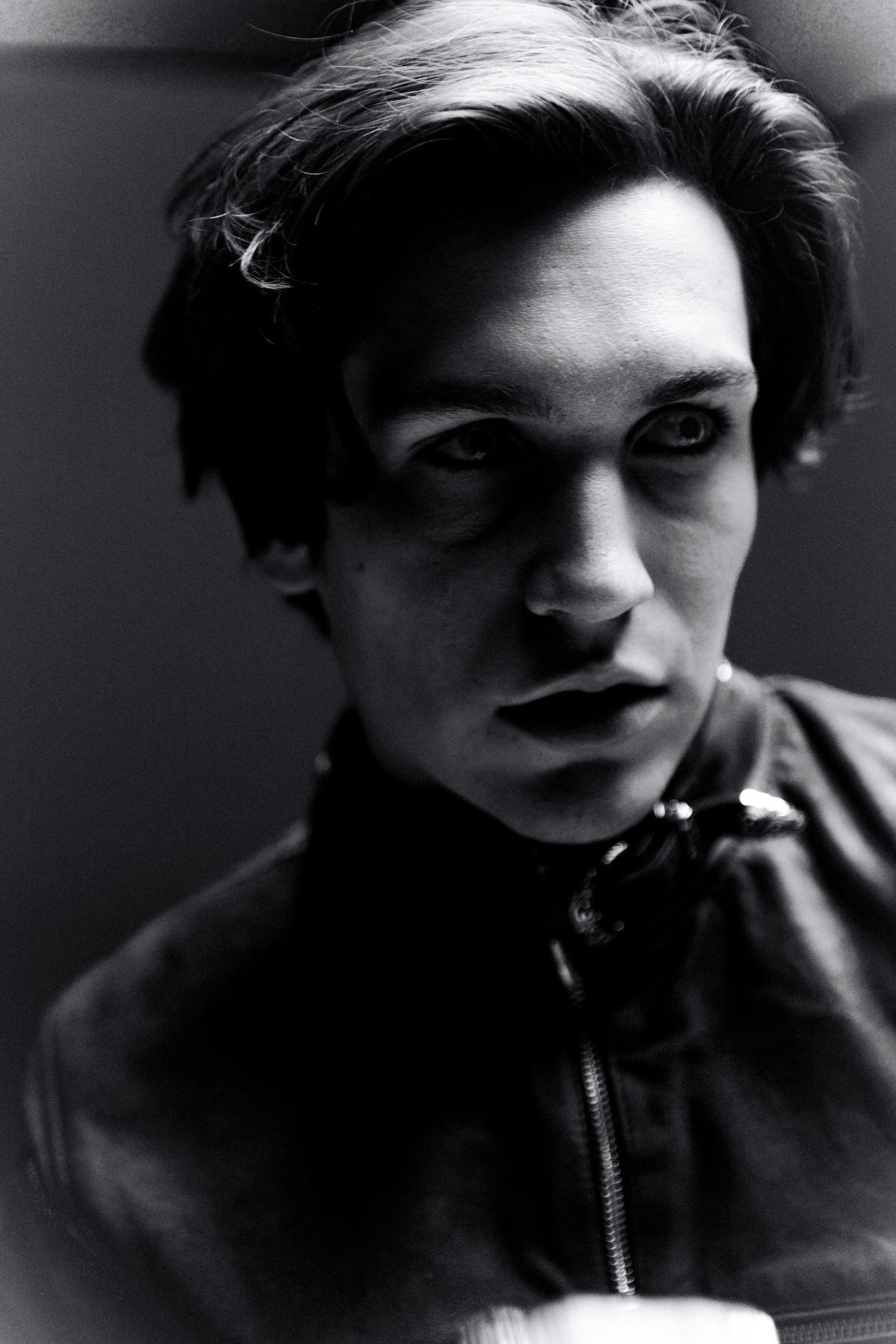 Close-up black and white photo of a young person's face, with focus on the eyes and hair, wearing a black jacket with a zipper.