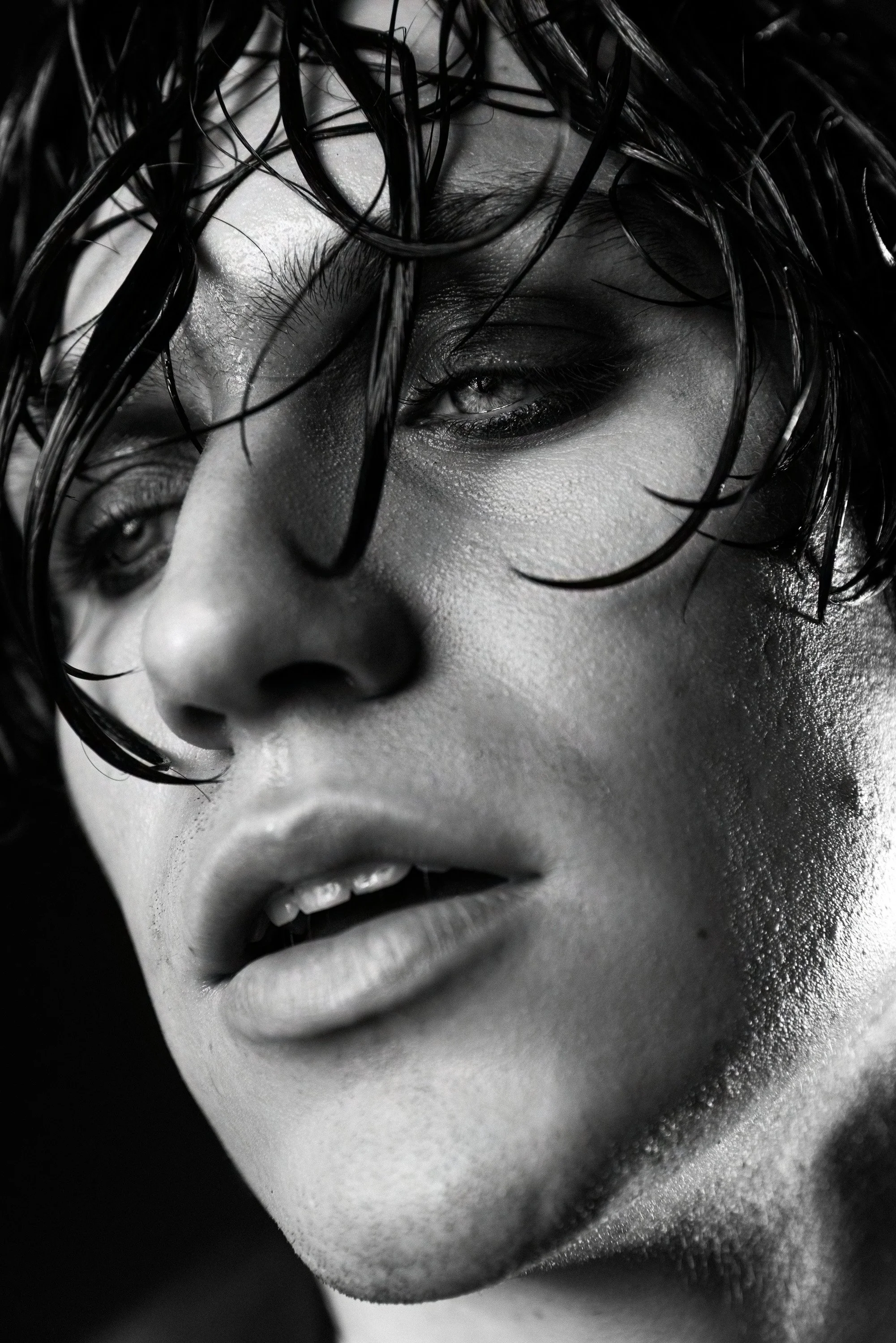 Close-up black and white photograph of a woman's face with wet hair partially covering her face, showing her eye, nose, and open lips.