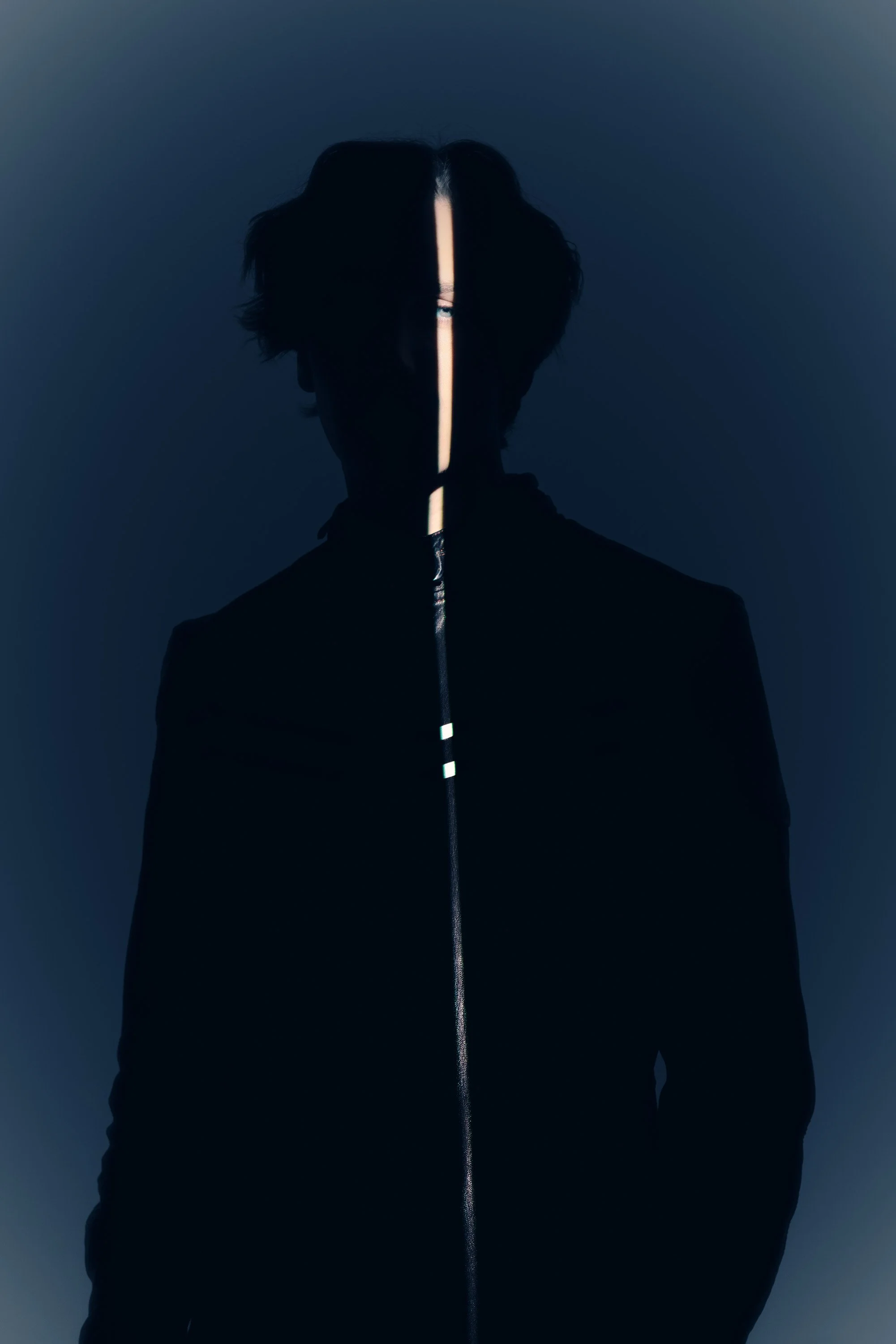 silhouette of a person with dark hair, facing forward, with a vertical strip of light illuminating the face.