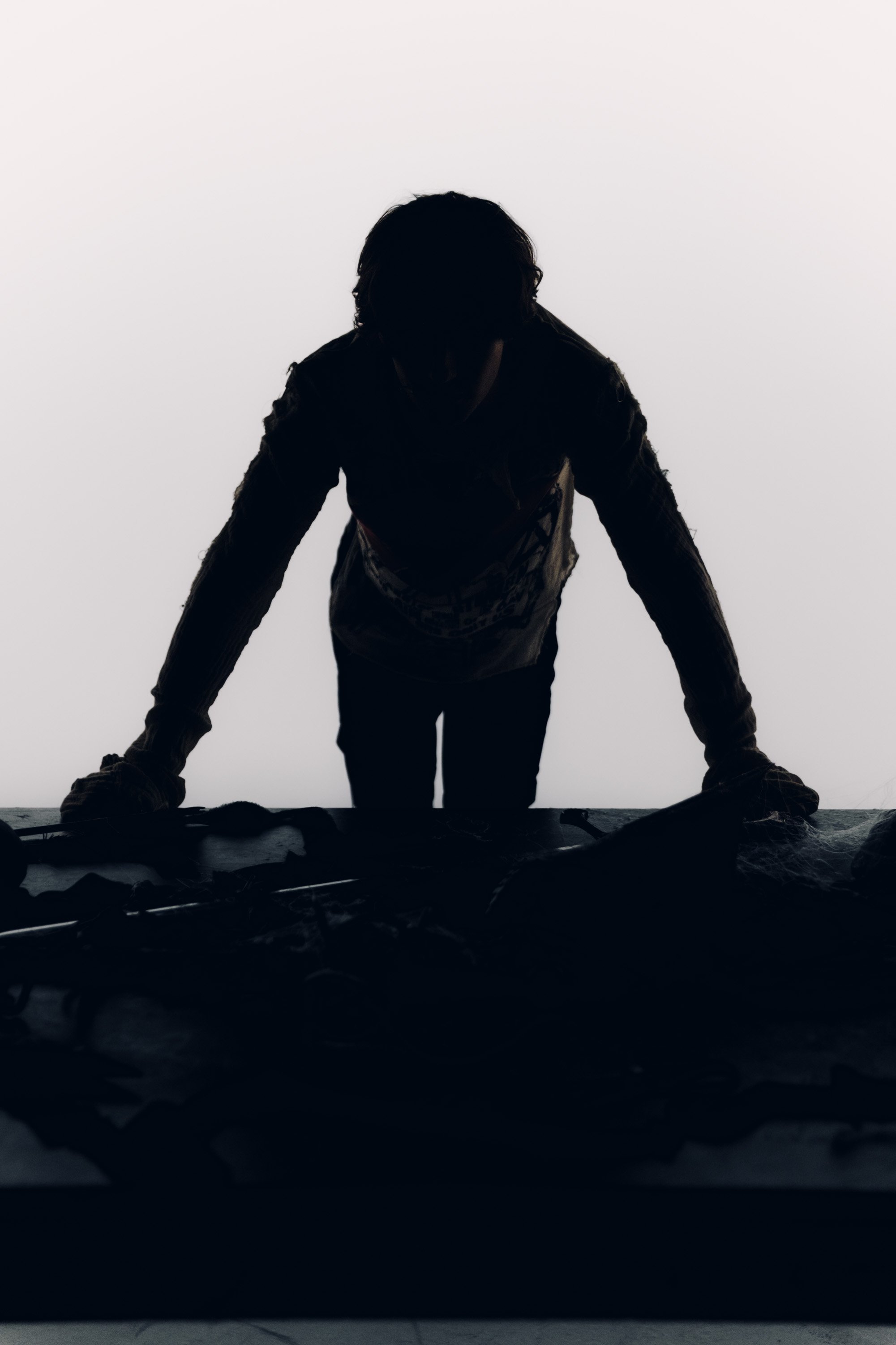 Silhouette of a person leaning forward against a surface with arms extended, with a plain light background.