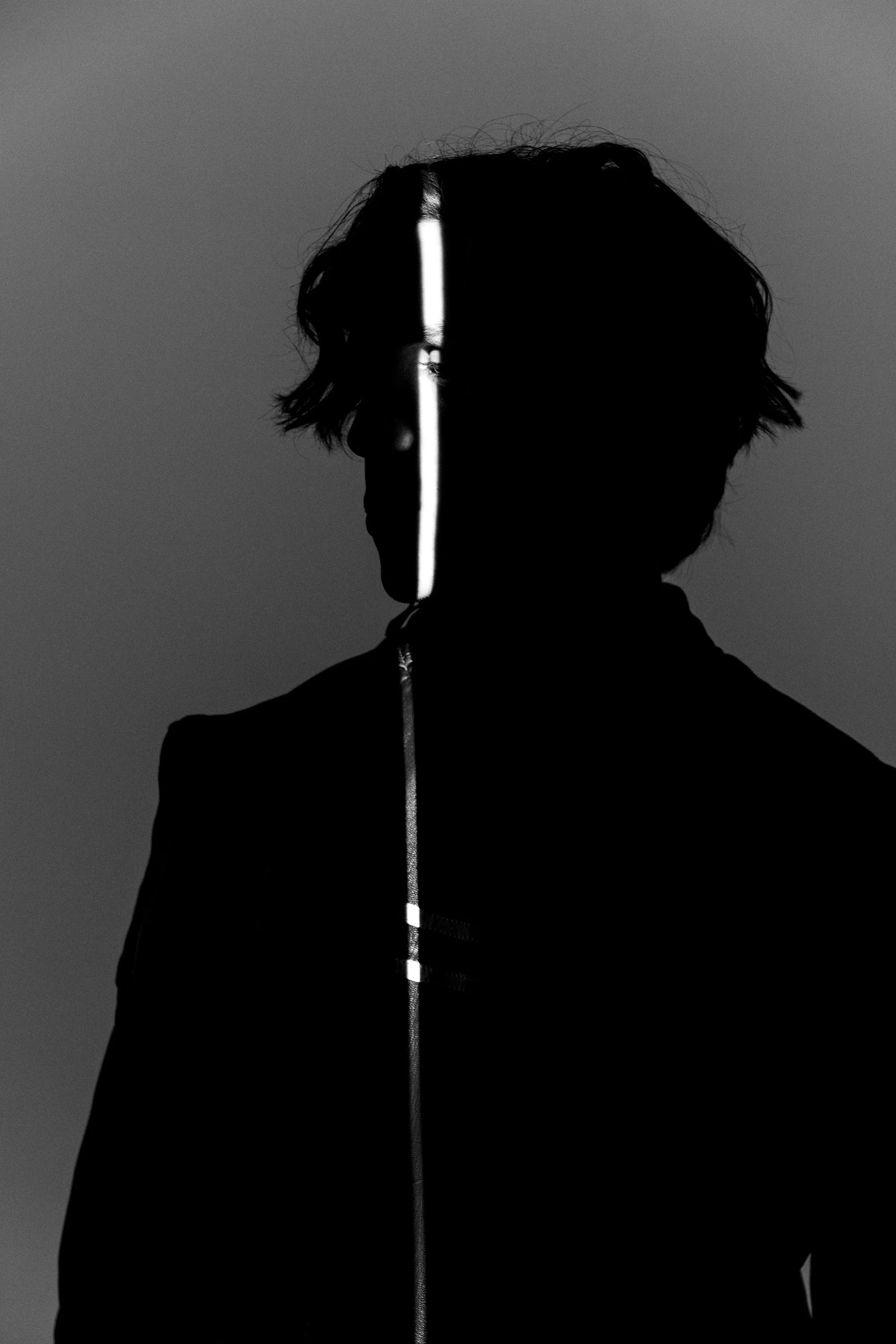 Silhouette of a person with partial light strip down the center of their face and body, dark background.