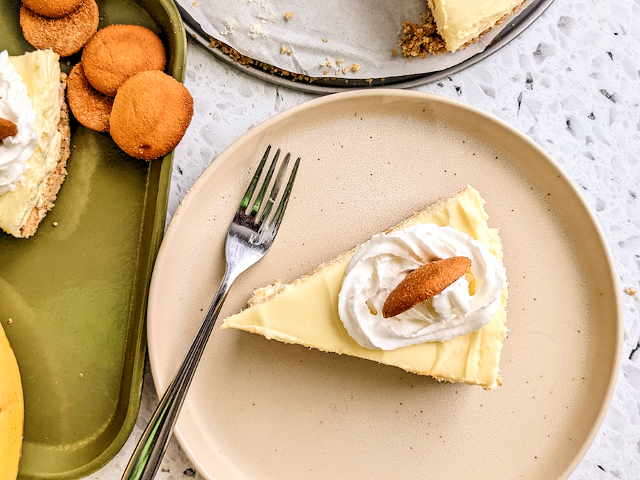 Slice of banana pudding cheese cake with whip cream and one vanilla wafer on top