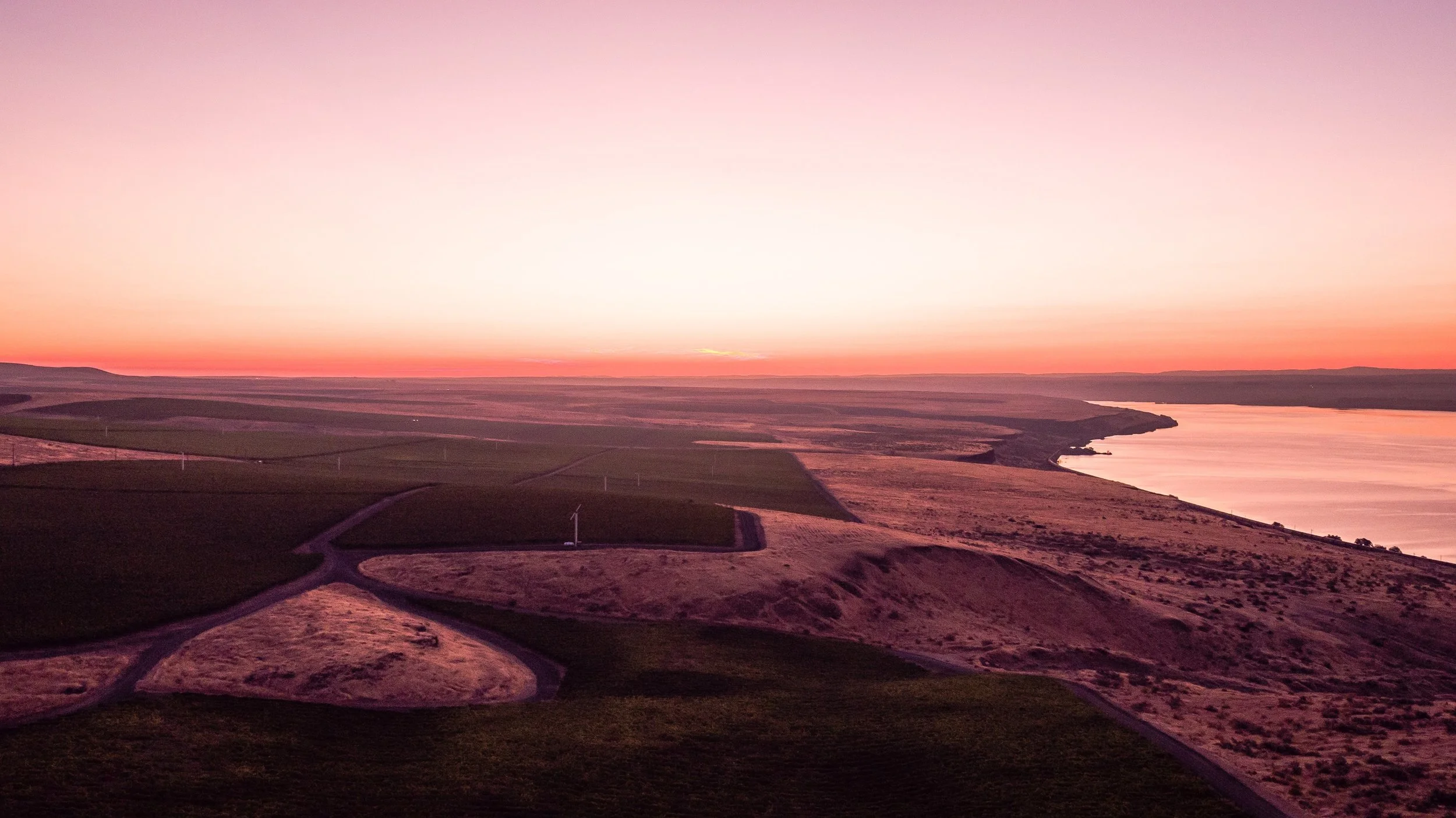 Sunset over a river with vineyards and winding roads in the foreground.