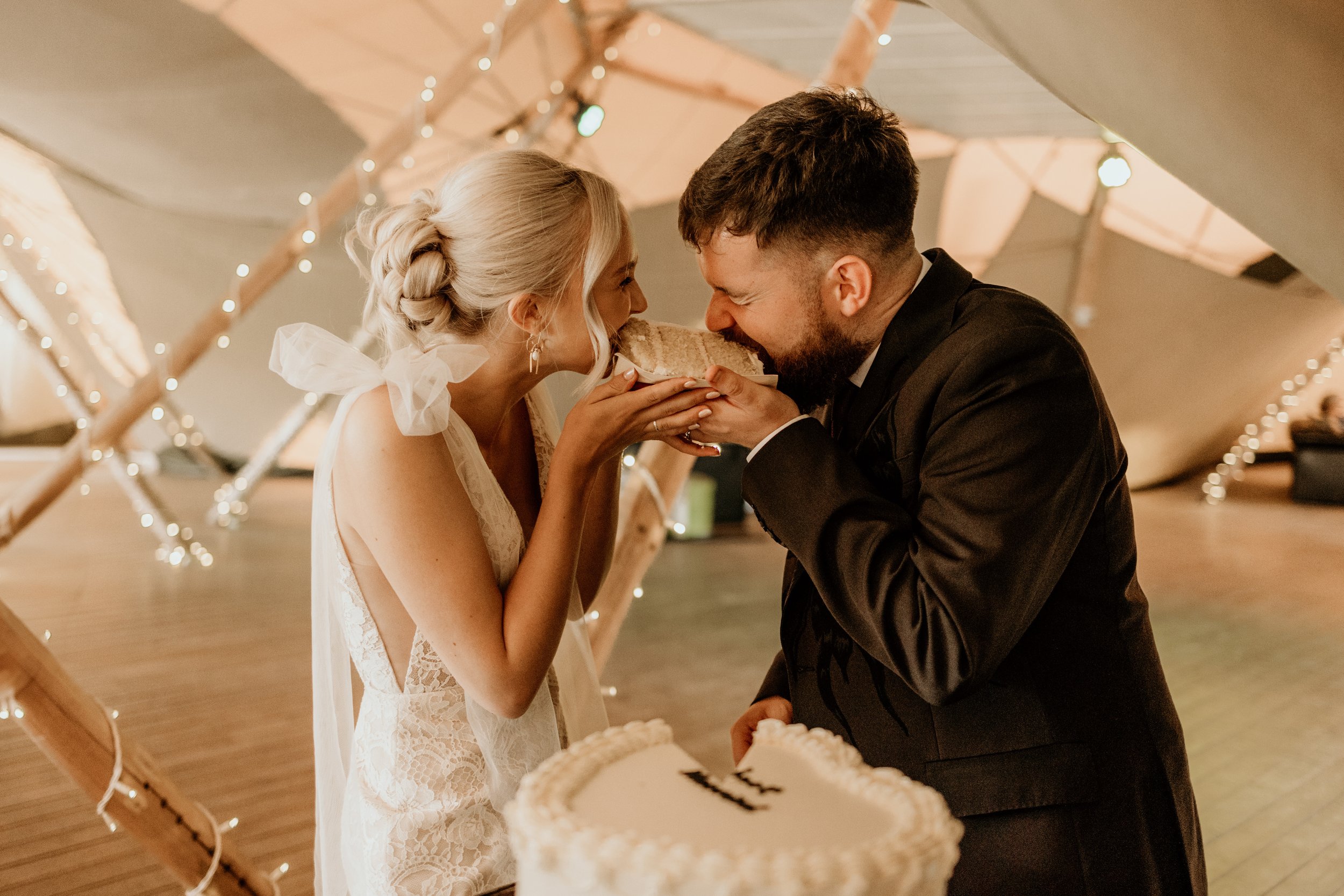 Relaxed wedding photography of the couple eating a slice of their cake together inside of their marquee