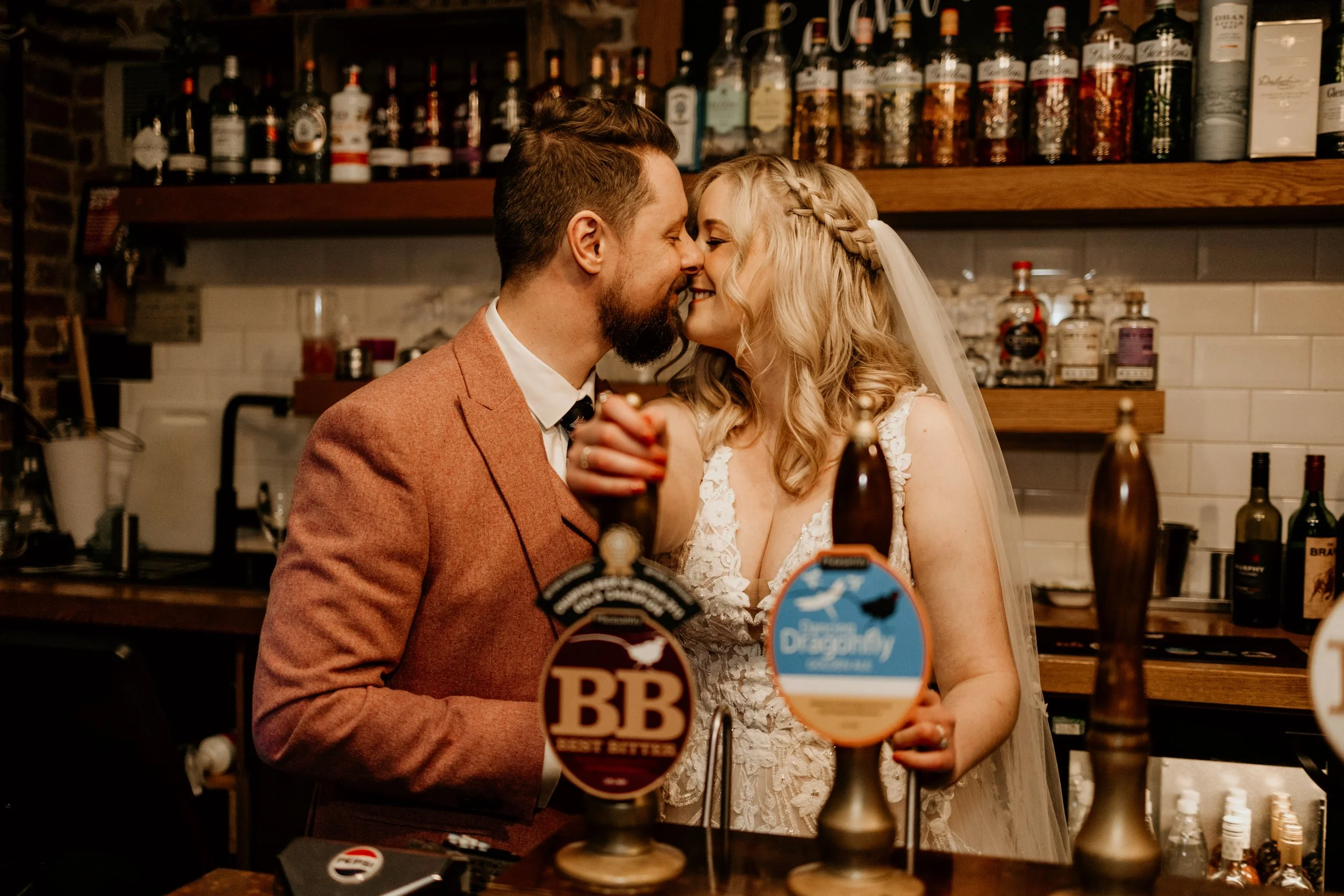 Relaxed wedding photography of couple about to kiss whilst pulling a point at a brewery wedding venue