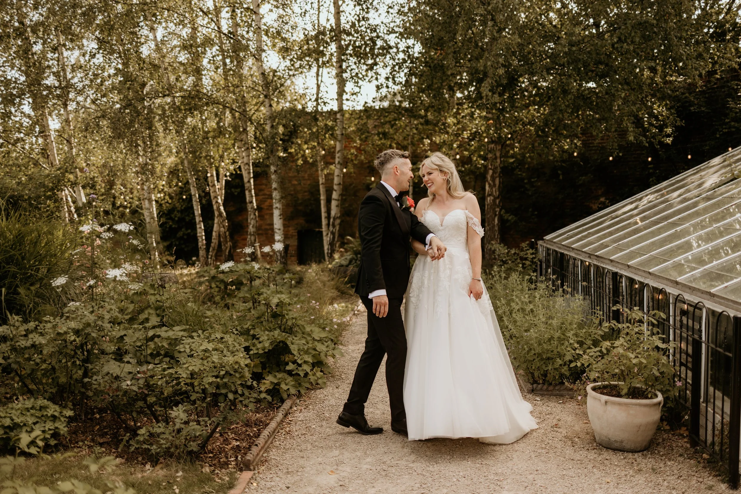 A relaxed wedding day shot of bride and groom holding hands smiling at each other outdoors at their wedding venue