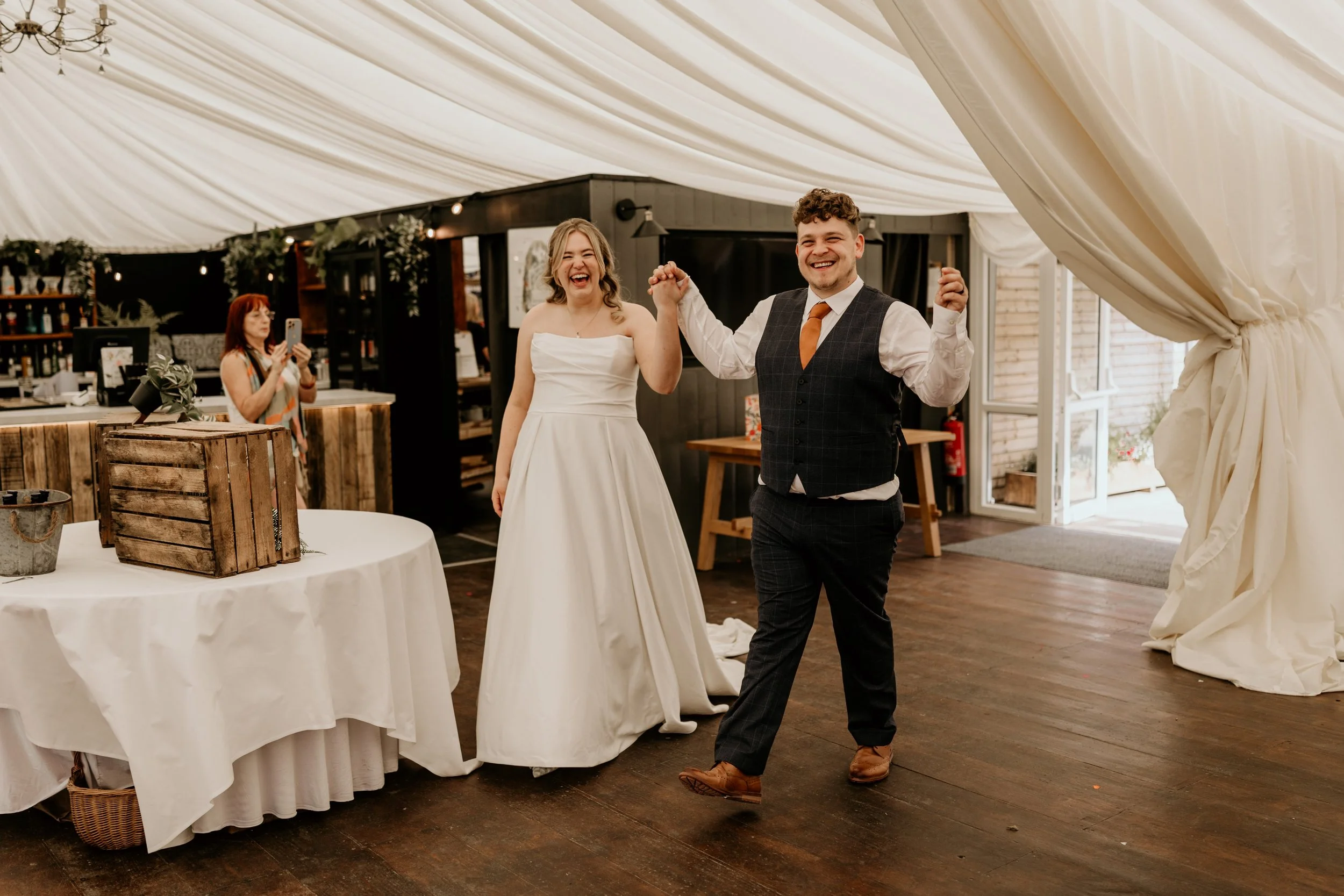 Relaxed wedding photography of couple holding hands smiling in their marquee