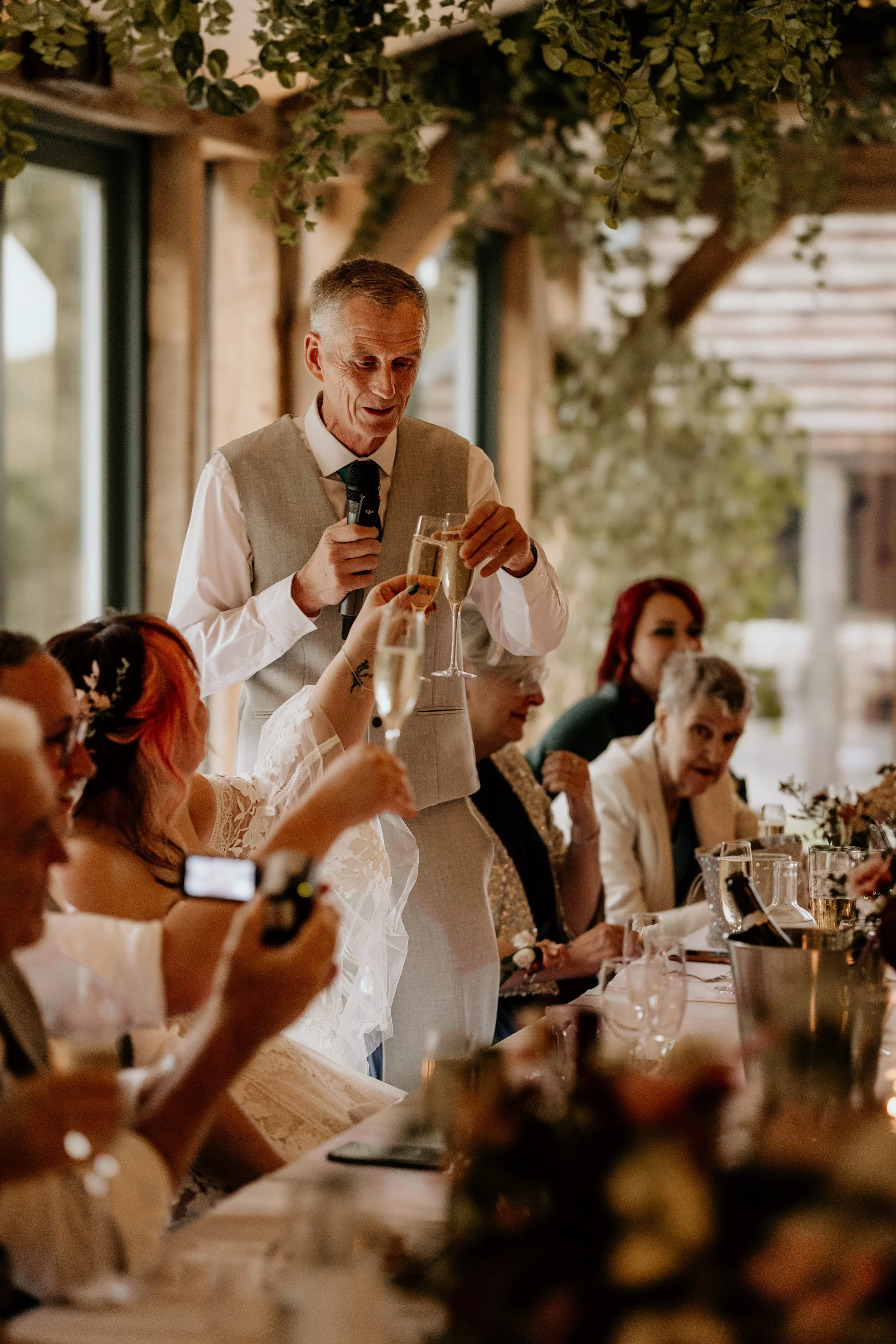 Relaxed wedding day shot of wedding guest holding glass of champagne making a toast