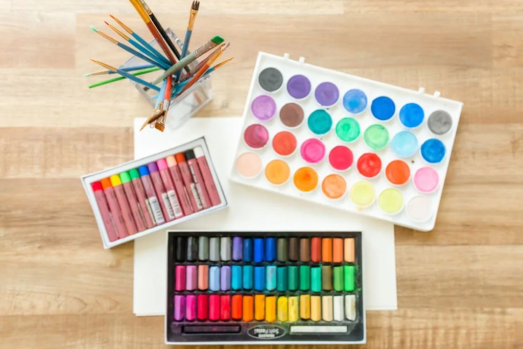 Colorful pastels, watercolor paints, pencils, and paper arranged for creative art journaling.