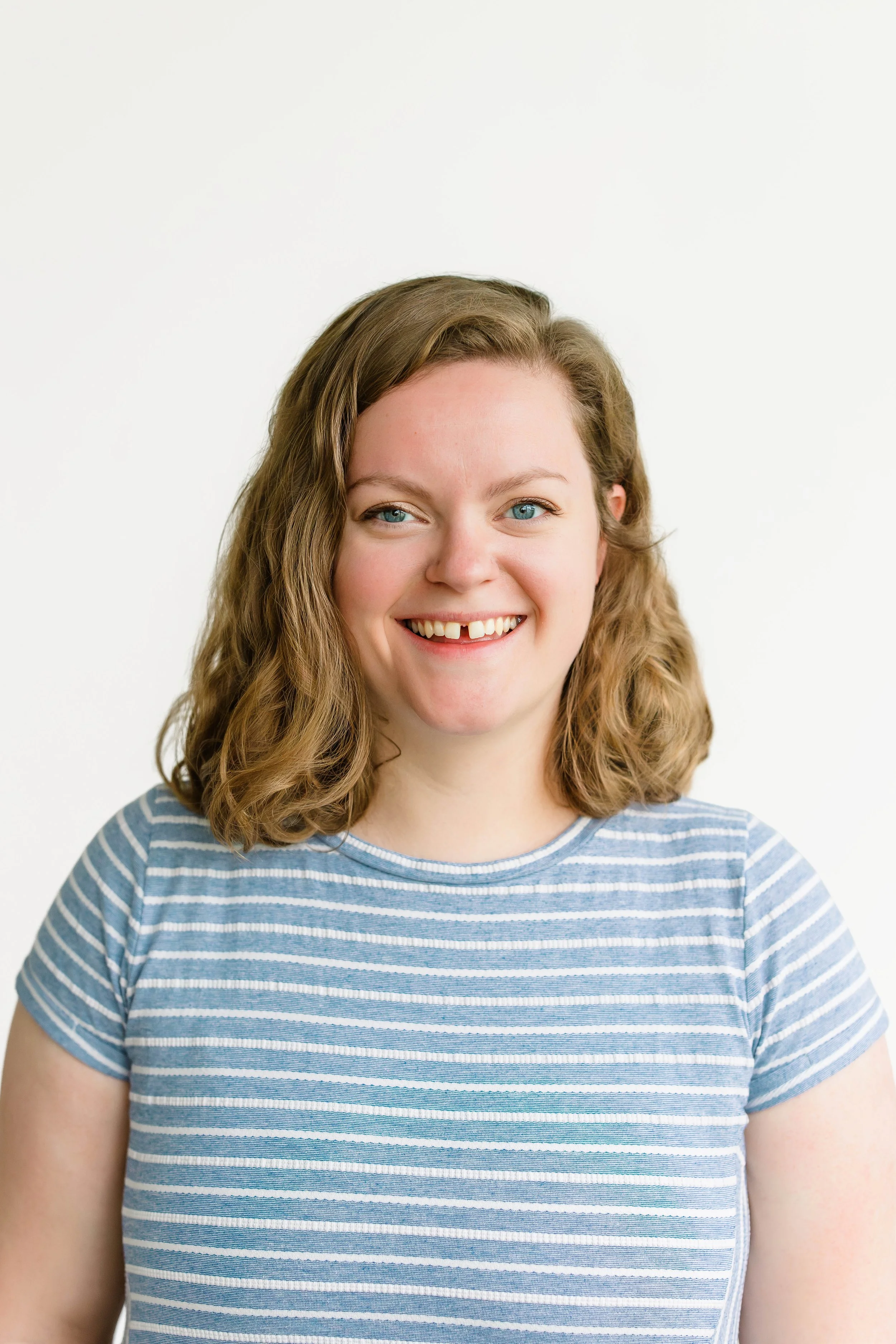 Headshot photo of a woman with curly brown hair and blue eyes, smiling, wearing a black top, against a plain white background.