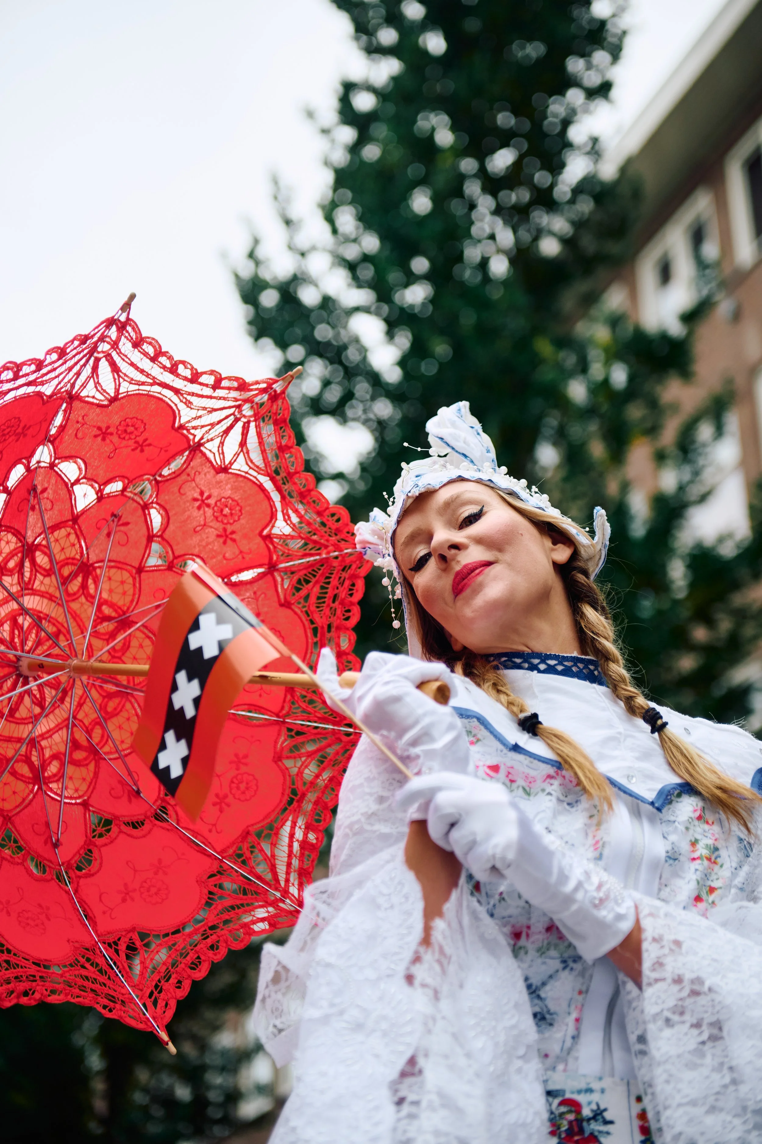 Woman dressed in traditional European folk costume holding a red decorative parasol and small Swiss flag outdoors.